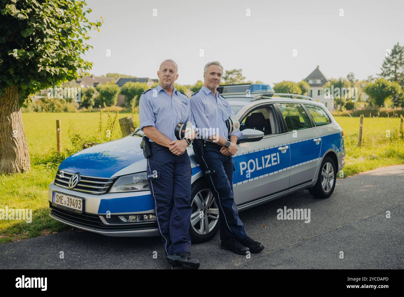 Colonia, Germania. 30 luglio 2024. Gli attori Heino Ferch (l) e Hannes Jaenicke stanno di fronte a un'auto della polizia durante le riprese. I due attori appaiono insieme davanti alla telecamera per la prima volta per la commedia ARD "Smeilingen". Credito: Marius Becker/dpa/Alamy Live News Foto Stock