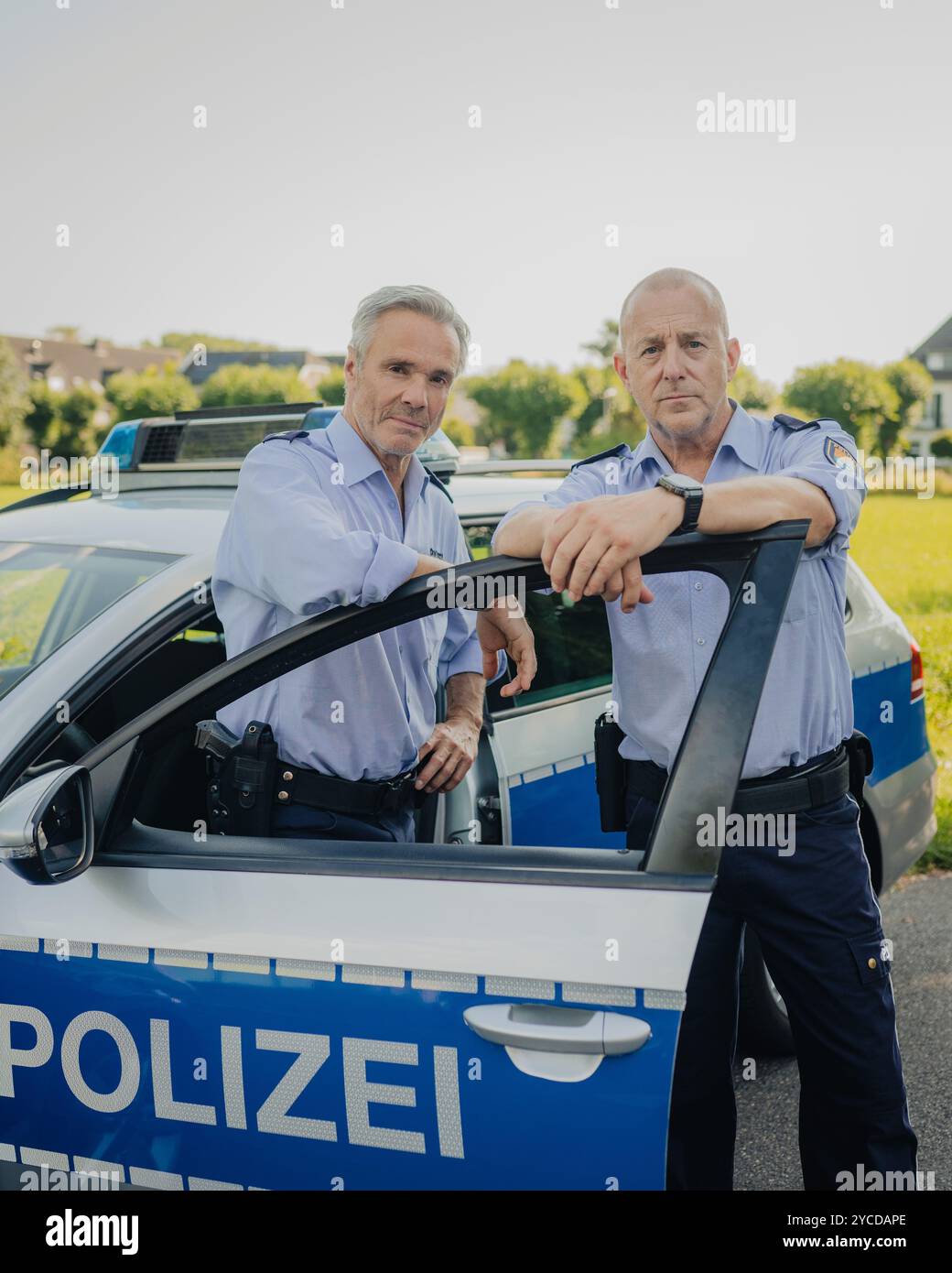 Colonia, Germania. 30 luglio 2024. Gli attori Heino Ferch (r) e Hannes Jaenicke stanno di fronte a un'auto della polizia durante le riprese. I due attori appaiono insieme davanti alla telecamera per la prima volta per la commedia ARD "Smeilingen". Credito: Marius Becker/dpa/Alamy Live News Foto Stock