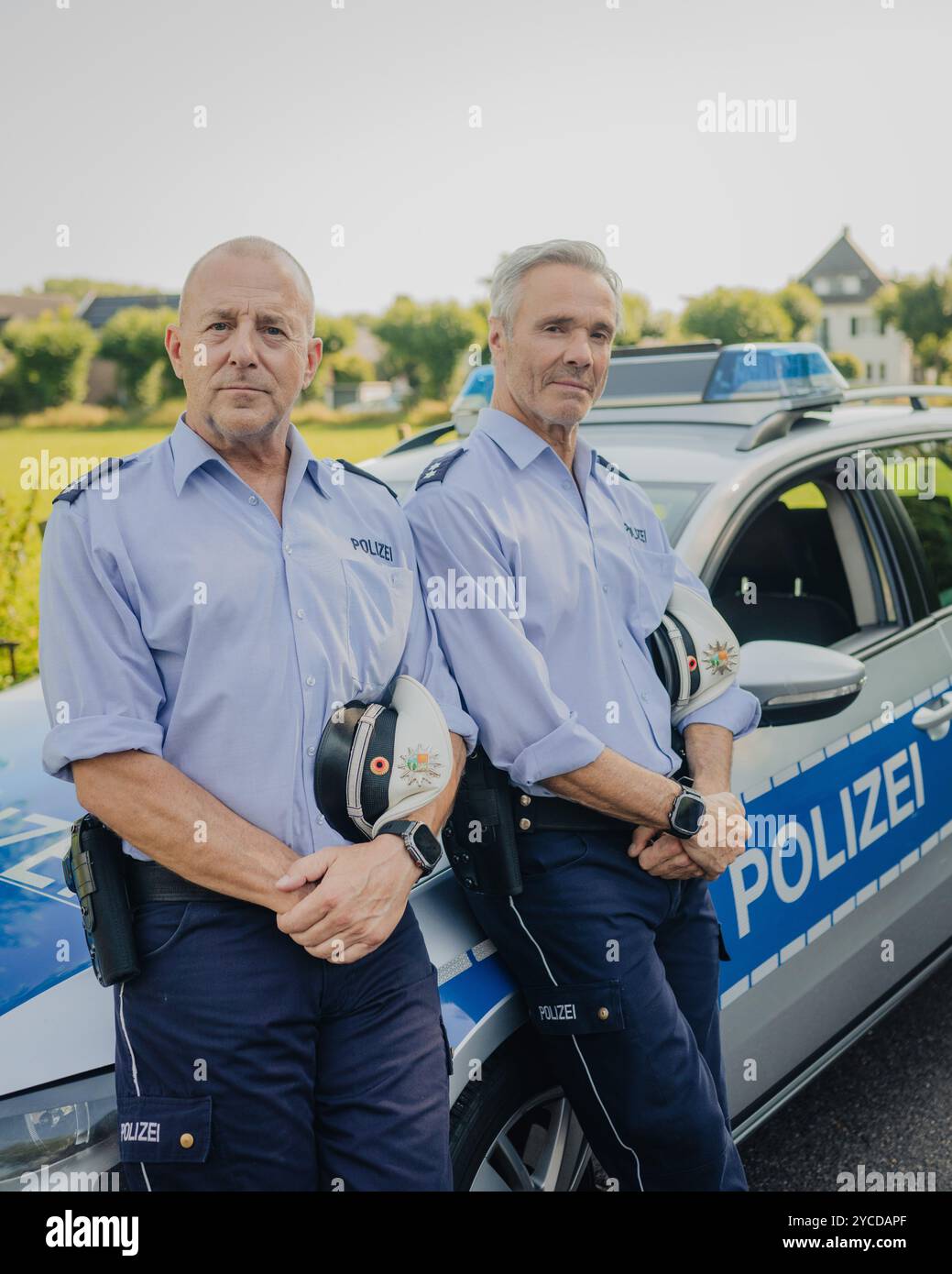 Colonia, Germania. 30 luglio 2024. Gli attori Heino Ferch (l) e Hannes Jaenicke stanno di fronte a un'auto della polizia durante le riprese. I due attori appaiono insieme davanti alla telecamera per la prima volta per la commedia ARD "Smeilingen". Credito: Marius Becker/dpa/Alamy Live News Foto Stock