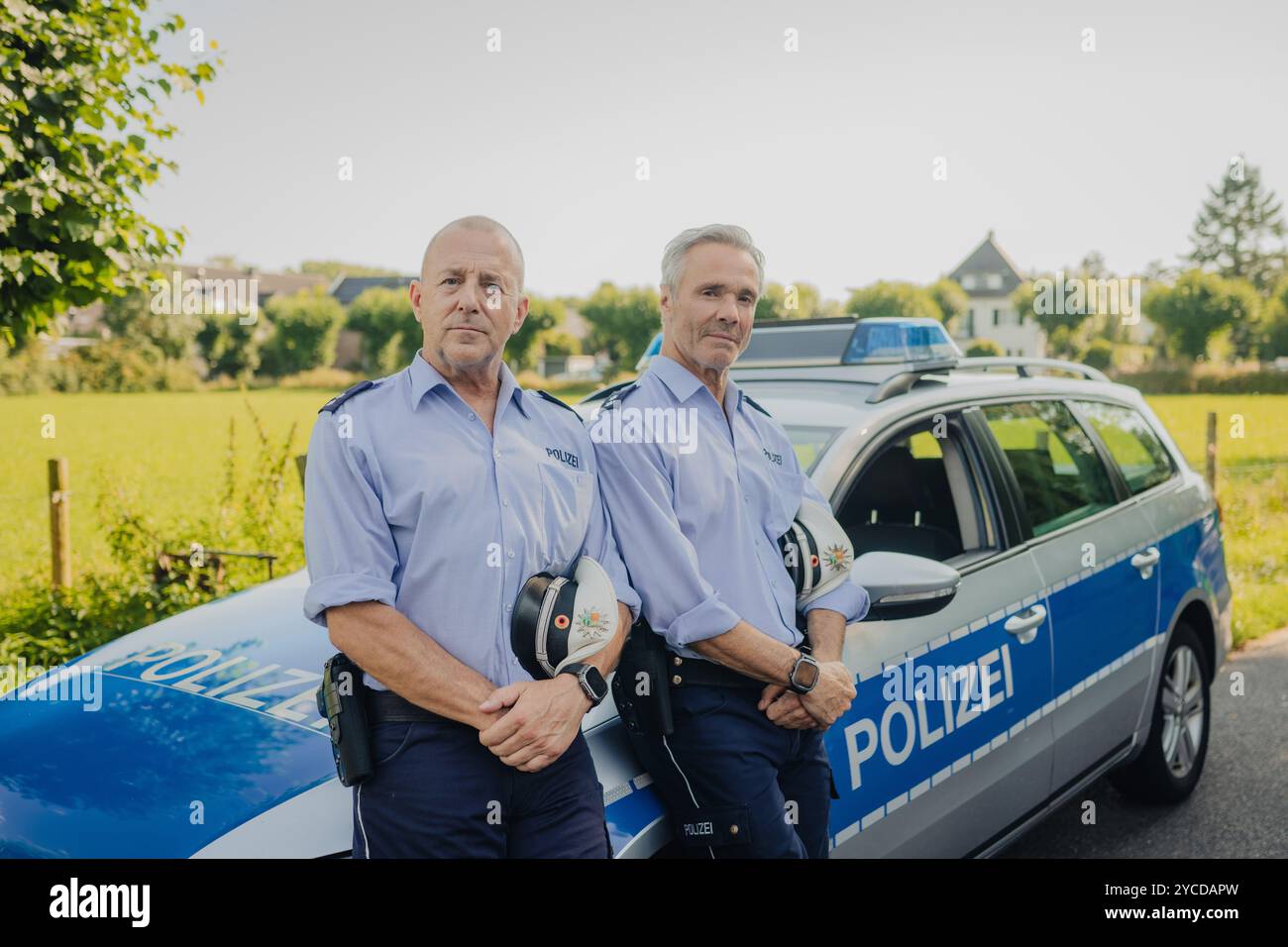 Colonia, Germania. 30 luglio 2024. Gli attori Heino Ferch (l) e Hannes Jaenicke stanno di fronte a un'auto della polizia durante le riprese. I due attori appaiono insieme davanti alla telecamera per la prima volta per la commedia ARD "Smeilingen". Credito: Marius Becker/dpa/Alamy Live News Foto Stock