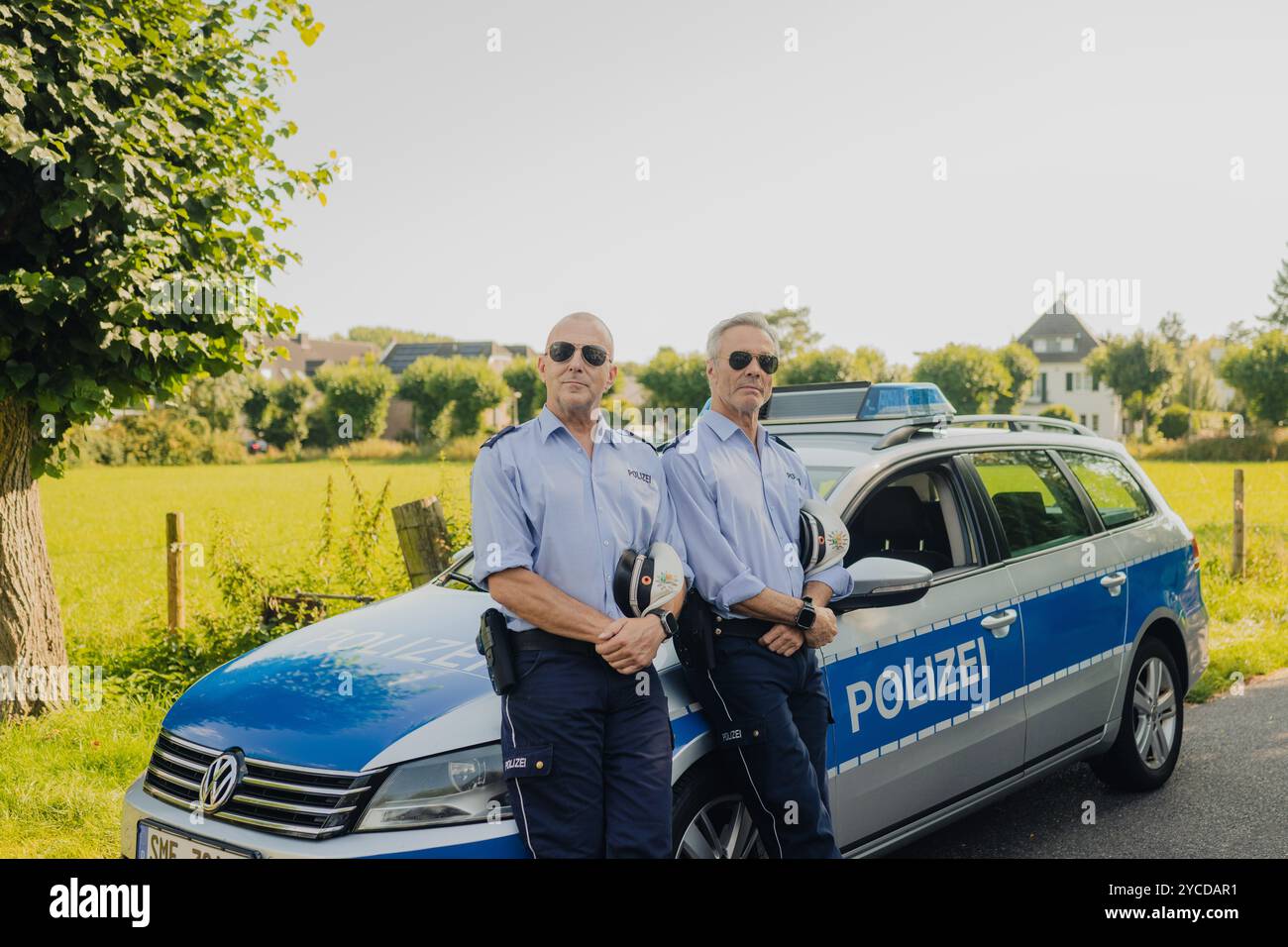 Colonia, Germania. 30 luglio 2024. Gli attori Heino Ferch (l) e Hannes Jaenicke stanno di fronte a un'auto della polizia durante le riprese. I due attori appaiono insieme davanti alla telecamera per la prima volta per la commedia ARD "Smeilingen". Credito: Marius Becker/dpa/Alamy Live News Foto Stock