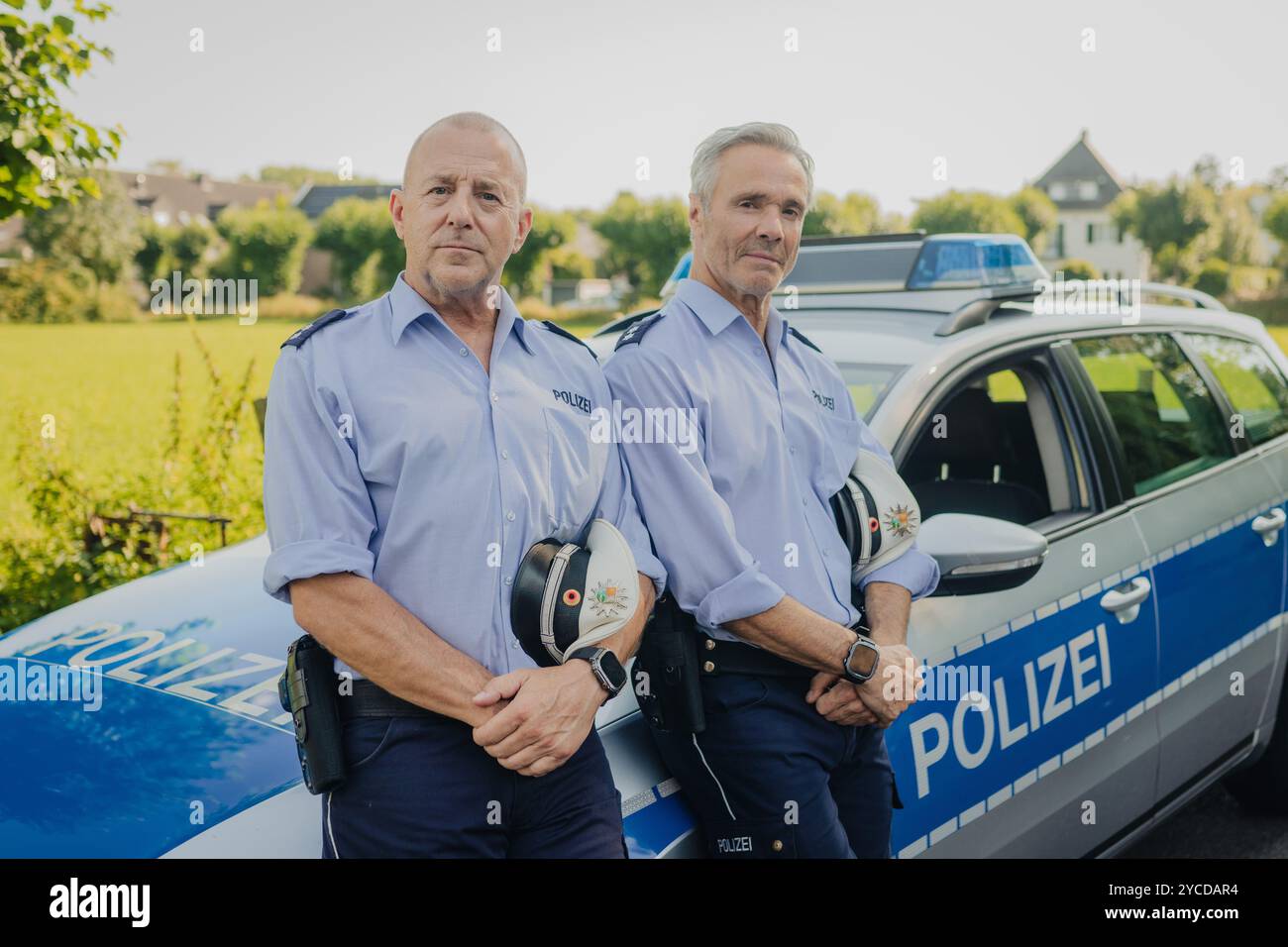 Colonia, Germania. 30 luglio 2024. Gli attori Heino Ferch (l) e Hannes Jaenicke stanno di fronte a un'auto della polizia durante le riprese. I due attori appaiono insieme davanti alla telecamera per la prima volta per la commedia ARD "Smeilingen". Credito: Marius Becker/dpa/Alamy Live News Foto Stock
