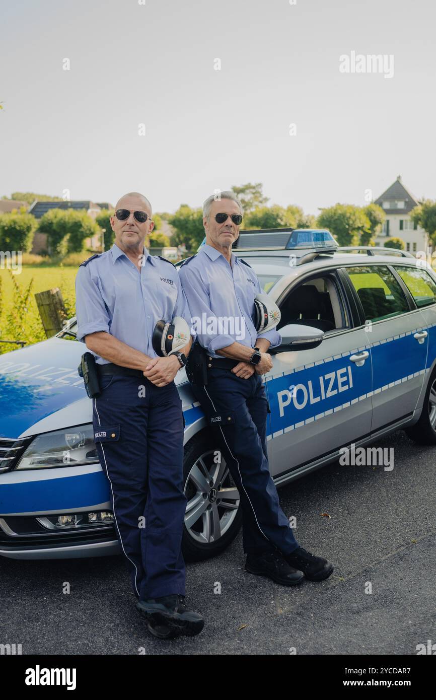 Colonia, Germania. 30 luglio 2024. Gli attori Heino Ferch (l) e Hannes Jaenicke stanno di fronte a un'auto della polizia durante le riprese. I due attori appaiono insieme davanti alla telecamera per la prima volta per la commedia ARD "Smeilingen". Credito: Marius Becker/dpa/Alamy Live News Foto Stock