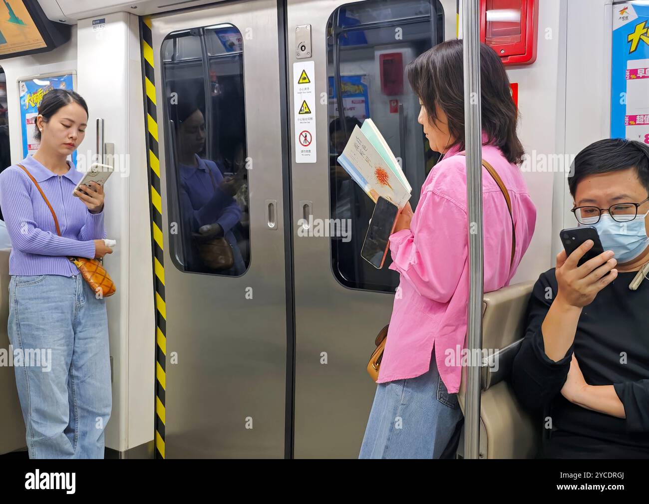 PECHINO, CINA - 13 OTTOBRE 2024 - lettori di libri cartacei e persone che guardano i telefoni cellulari su una metropolitana a Pechino, Cina, 13 settembre 2024. Foto Stock