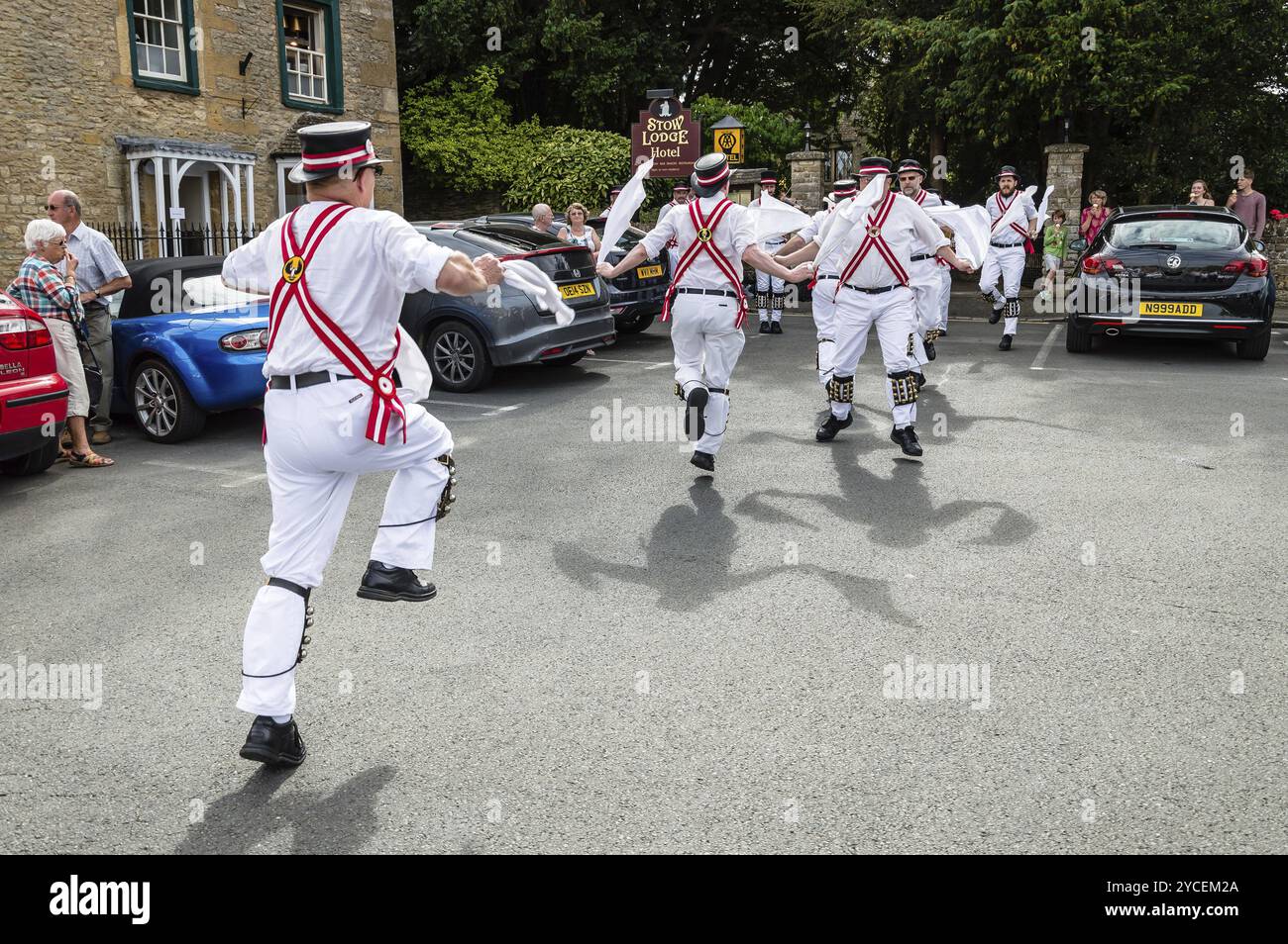 Stow on the Wold, Regno Unito, 12 agosto 2015: I Morris Dancers ballano in una piazza del villaggio di Stow on the Wold nei Cotswolds, mentre alcuni turisti lo sono Foto Stock