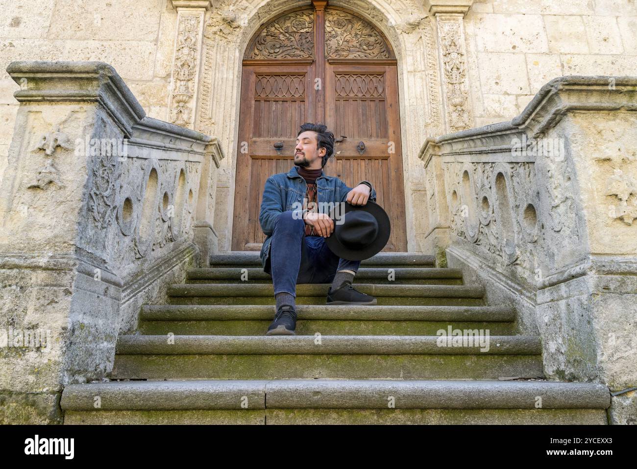 Ritratto di un giovane uomo seduto contro una bella e antica cattedrale medievale porta. Un uomo di fronte a un'architettura antica chiesa porta di ingresso in Alba Foto Stock