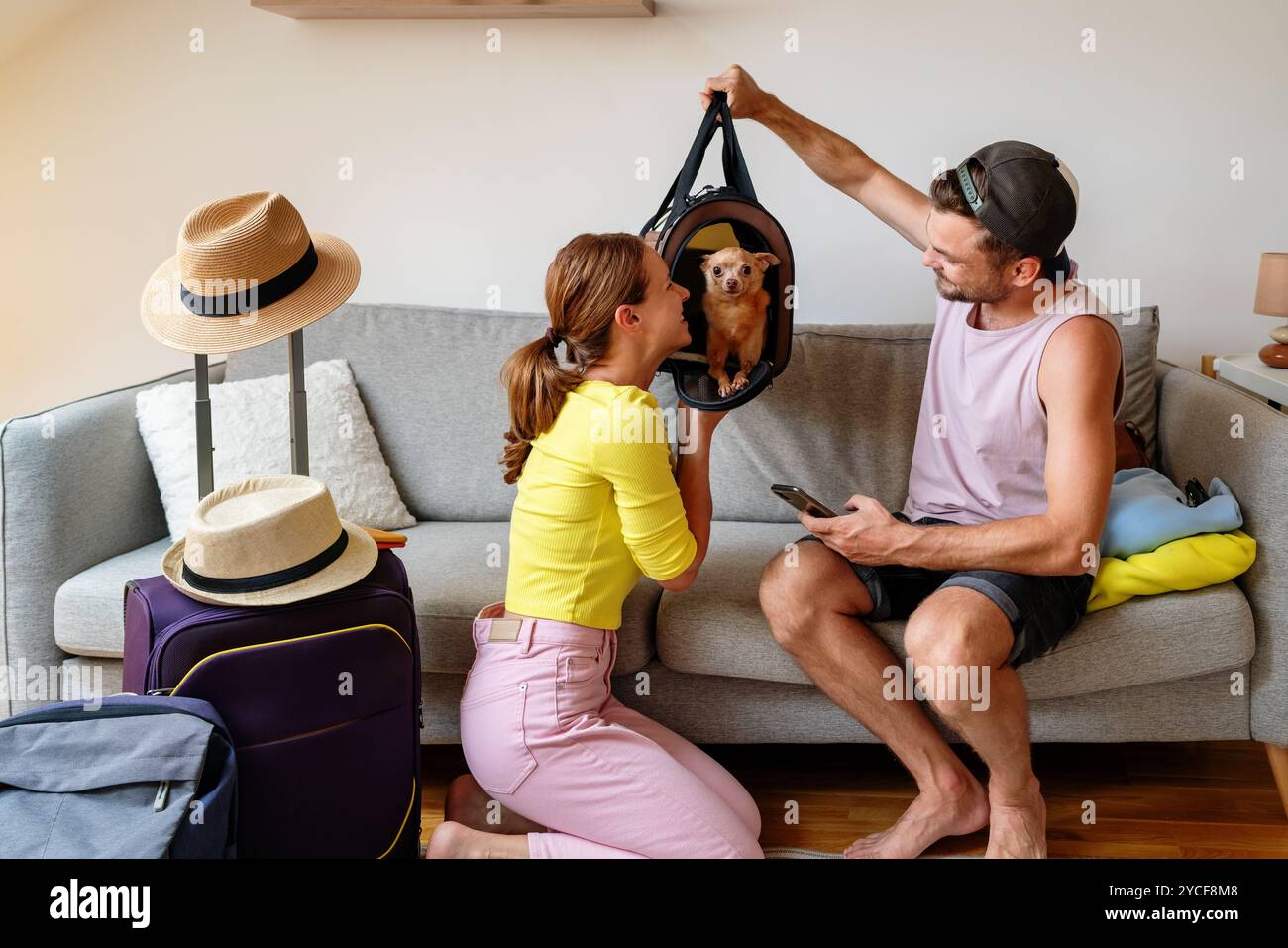 Giovane coppia a casa che si prepara a viaggiare con il loro piccolo cane in un portabagagli. Foto Stock