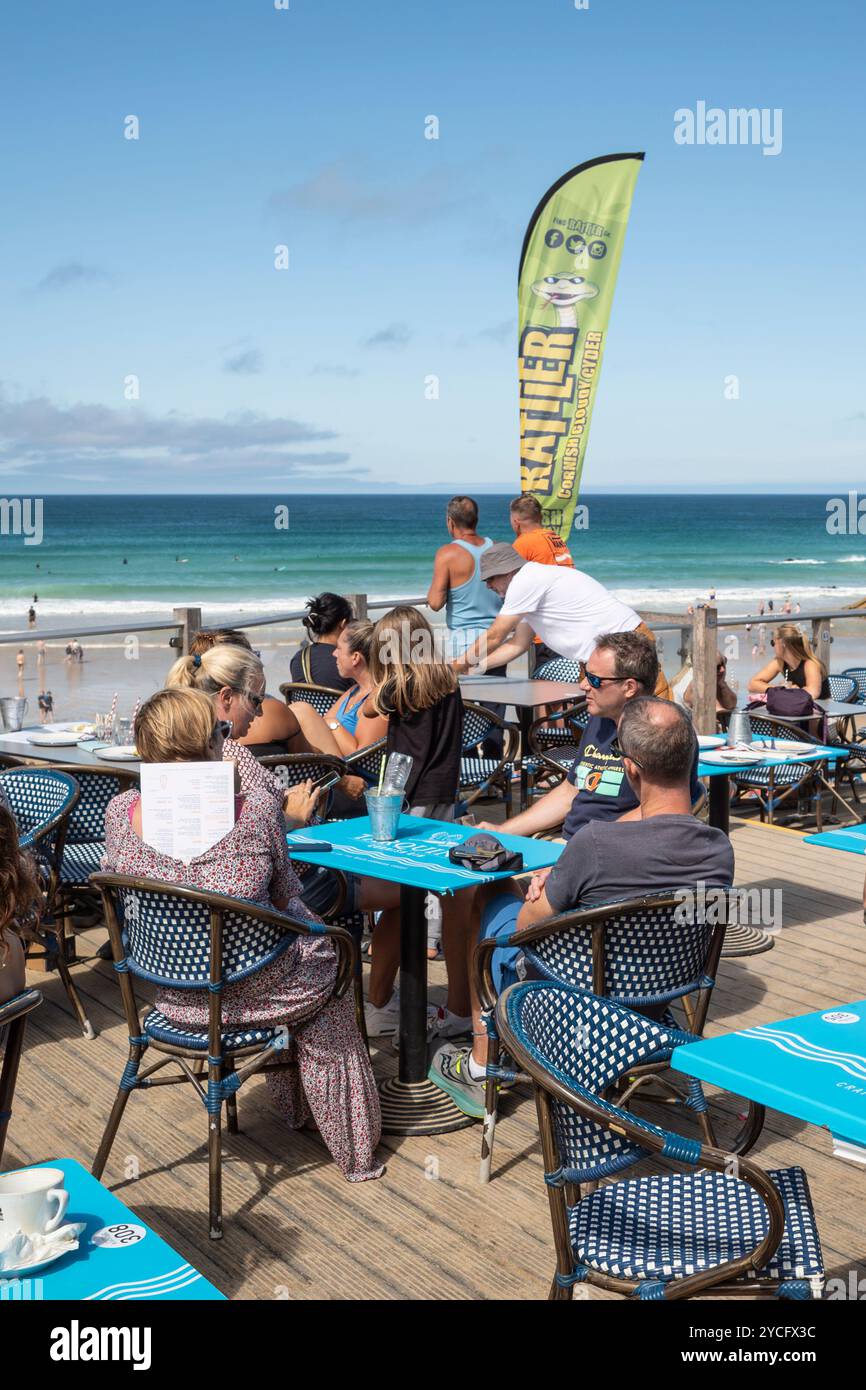 I vacanzieri si godono il sole estivo seduto sulla terrazza all'aperto del Fistral Beach Bar di Newquay in Cornovaglia nel Regno Unito. Foto Stock