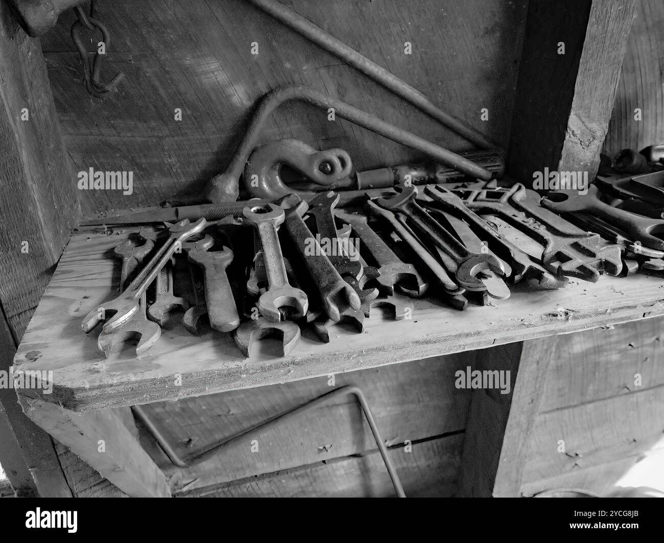 Grande gruppo di utensili metallici, principalmente chiavi o chiavi, impilati su un banco di lavoro in legno in una capanna di legno, nera e bianca. Atmosfera vintage. Foto Stock