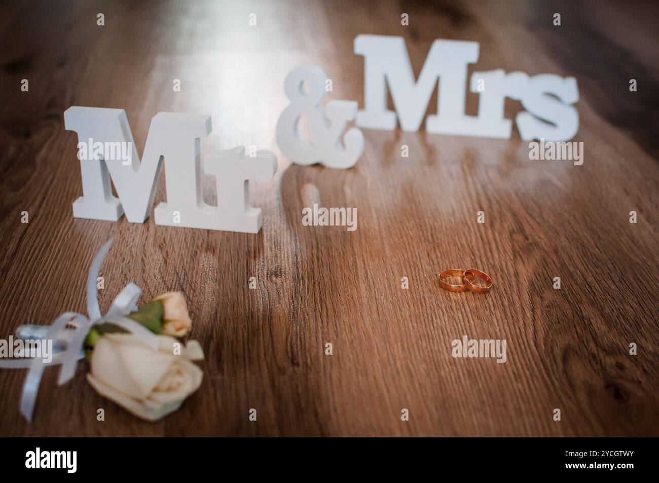 Eleganti simboli di matrimonio con anelli e accento floreale su pavimento in legno. Foto Stock