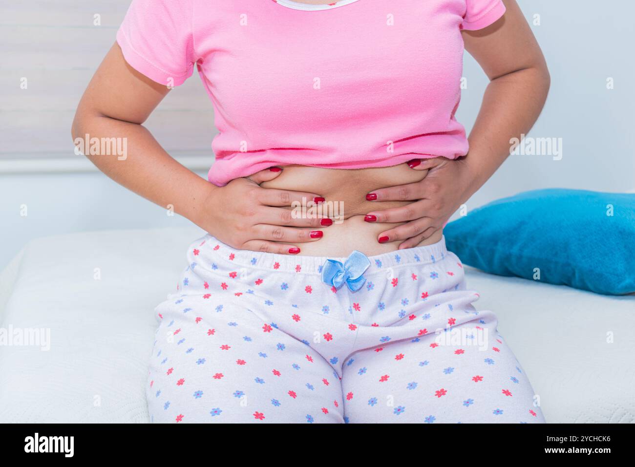 Una donna tocca il suo addome seduto sul letto; i crampi mestruali sono comuni ogni mese nelle donne in età fertile. Primo piano. Foto Stock