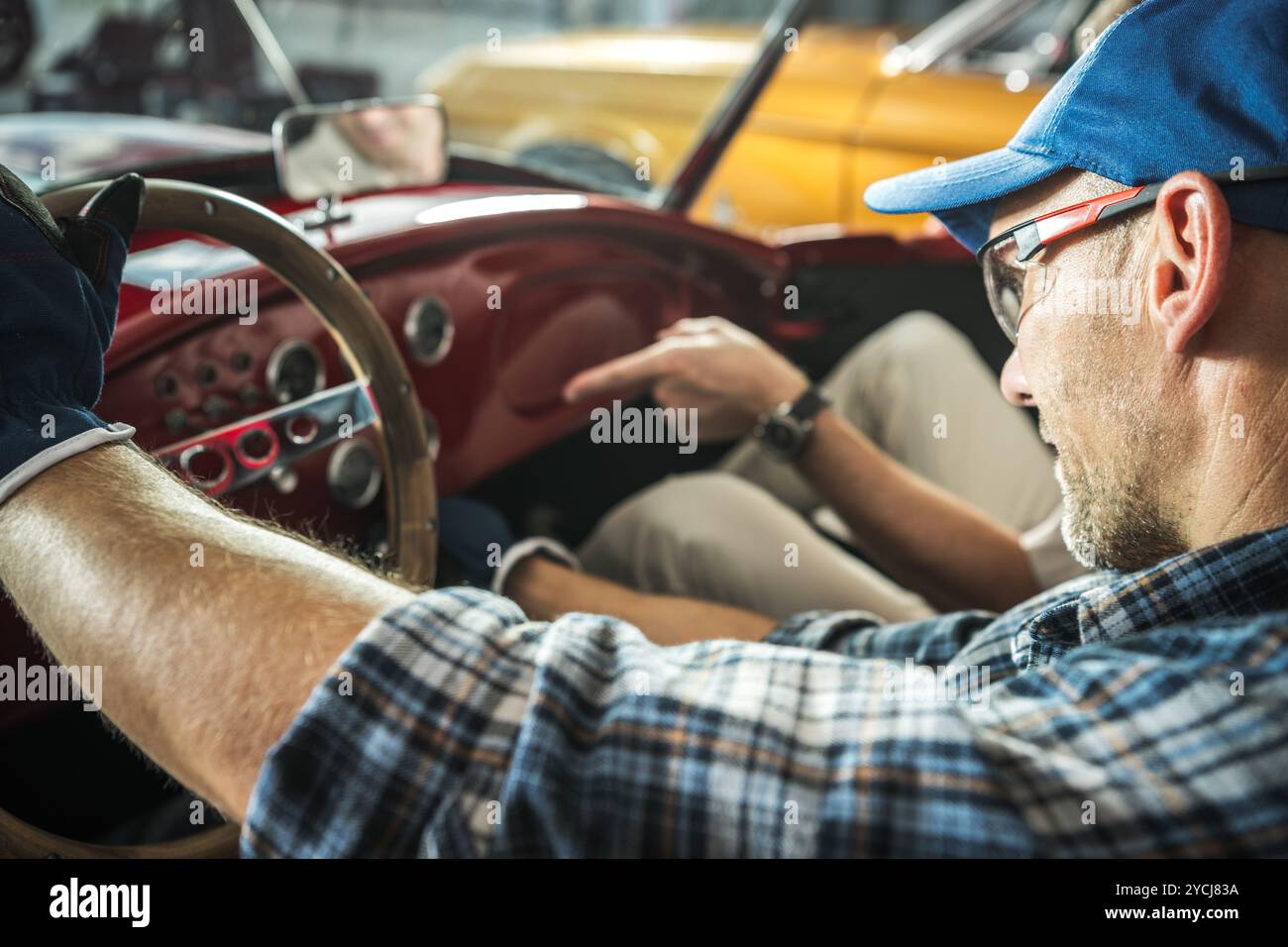 Un appassionato di auto ispeziona i componenti del cruscotto mentre lavora su un'auto d'epoca in un garage. L'atmosfera rivela la passione per il restauro delle automobili Foto Stock