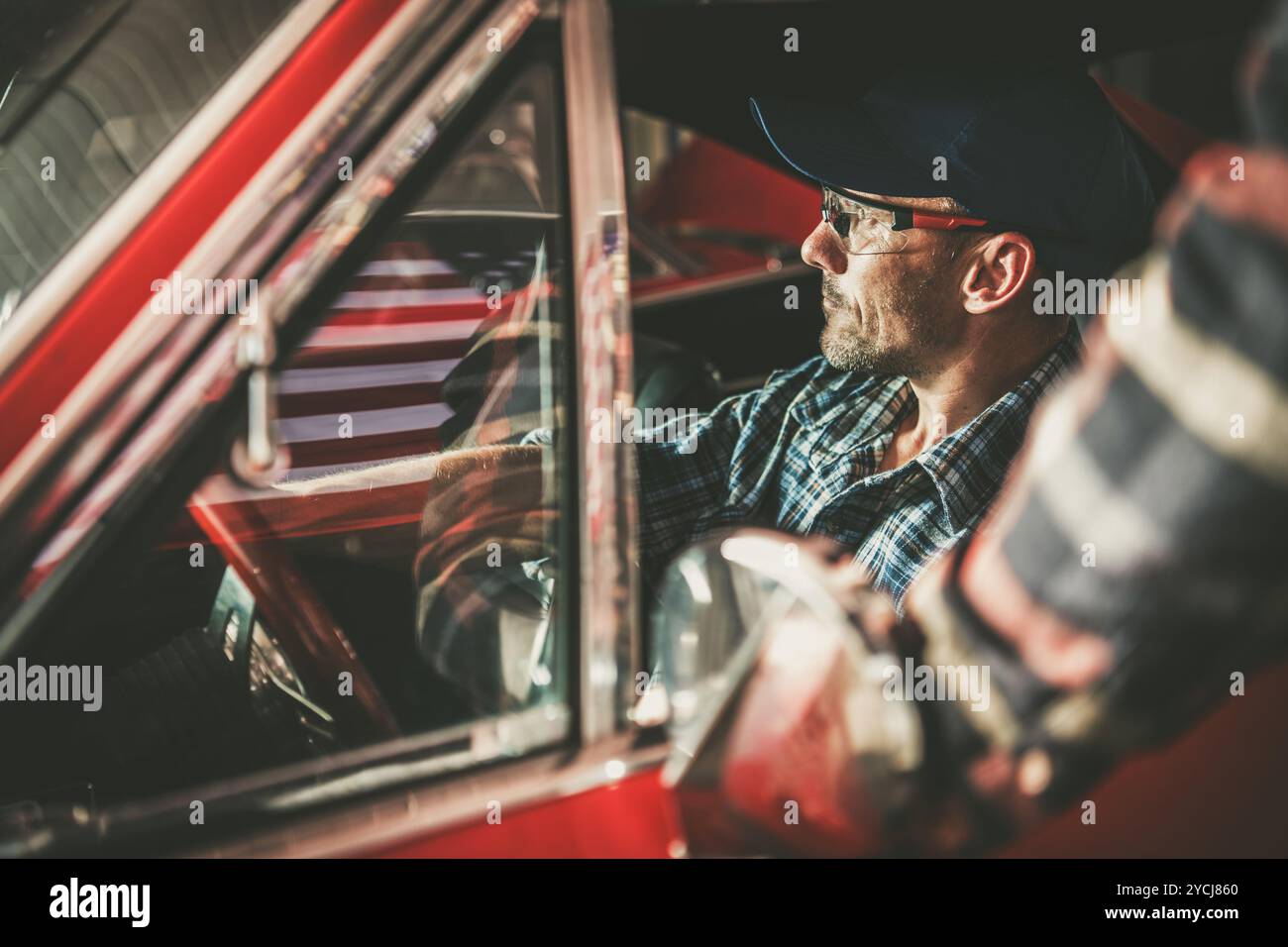 Un uomo con occhiali si concentra all'interno di un'auto d'epoca, preparandosi per i lavori di restauro in un garage, mostrando la sua dedizione e i suoi artigiani Foto Stock