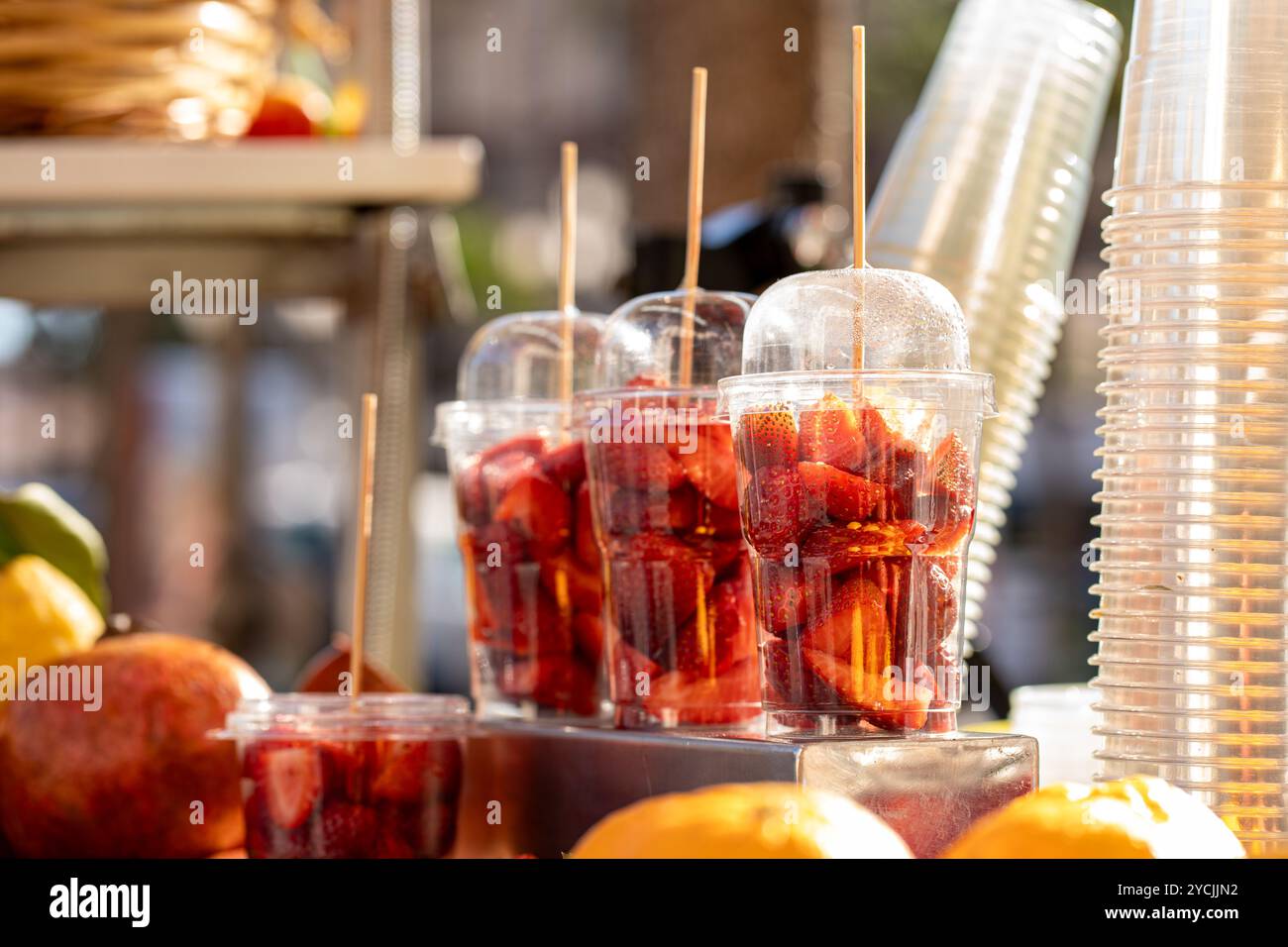 Fragole fresche tagliate in tazze di plastica monouso con bastoncini di legno. Sano spuntino di Street food al mercato locale. Frutta estiva pronta da mangiare con spirito Foto Stock