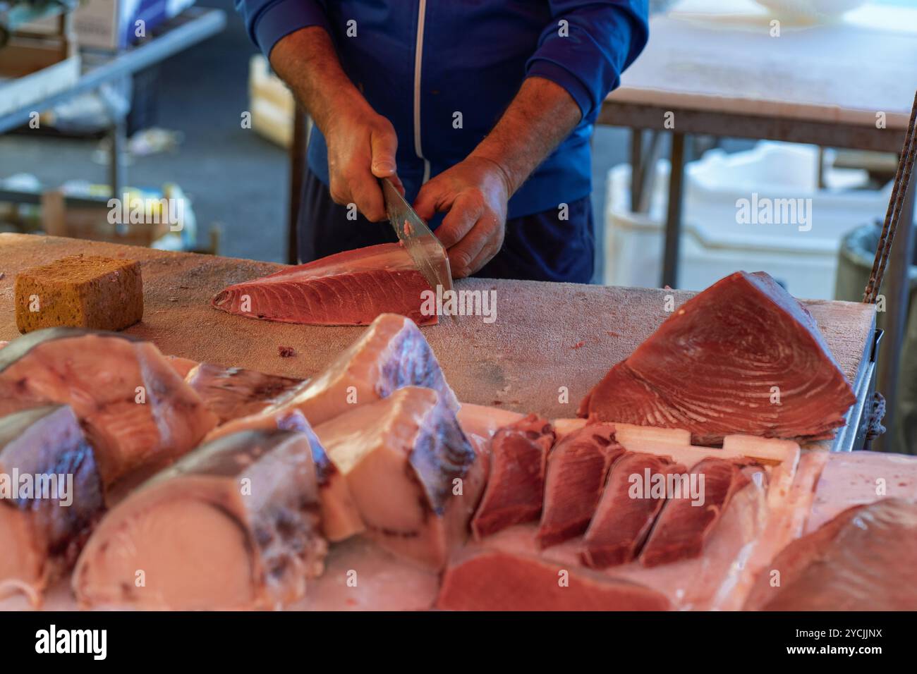 Pescivendolo professionale che affetta il tonno crudo fresco al mercato locale. Tradizionale tecnica di preparazione del pesce mediterraneo presso la storica marga di pesce di Catania Foto Stock