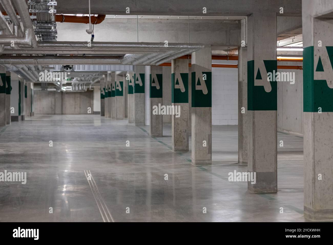 Moderno parcheggio sotterraneo con colonne in cemento, condotti di ventilazione e segnali di uscita verdi, con spazio vuoto organizzato Foto Stock