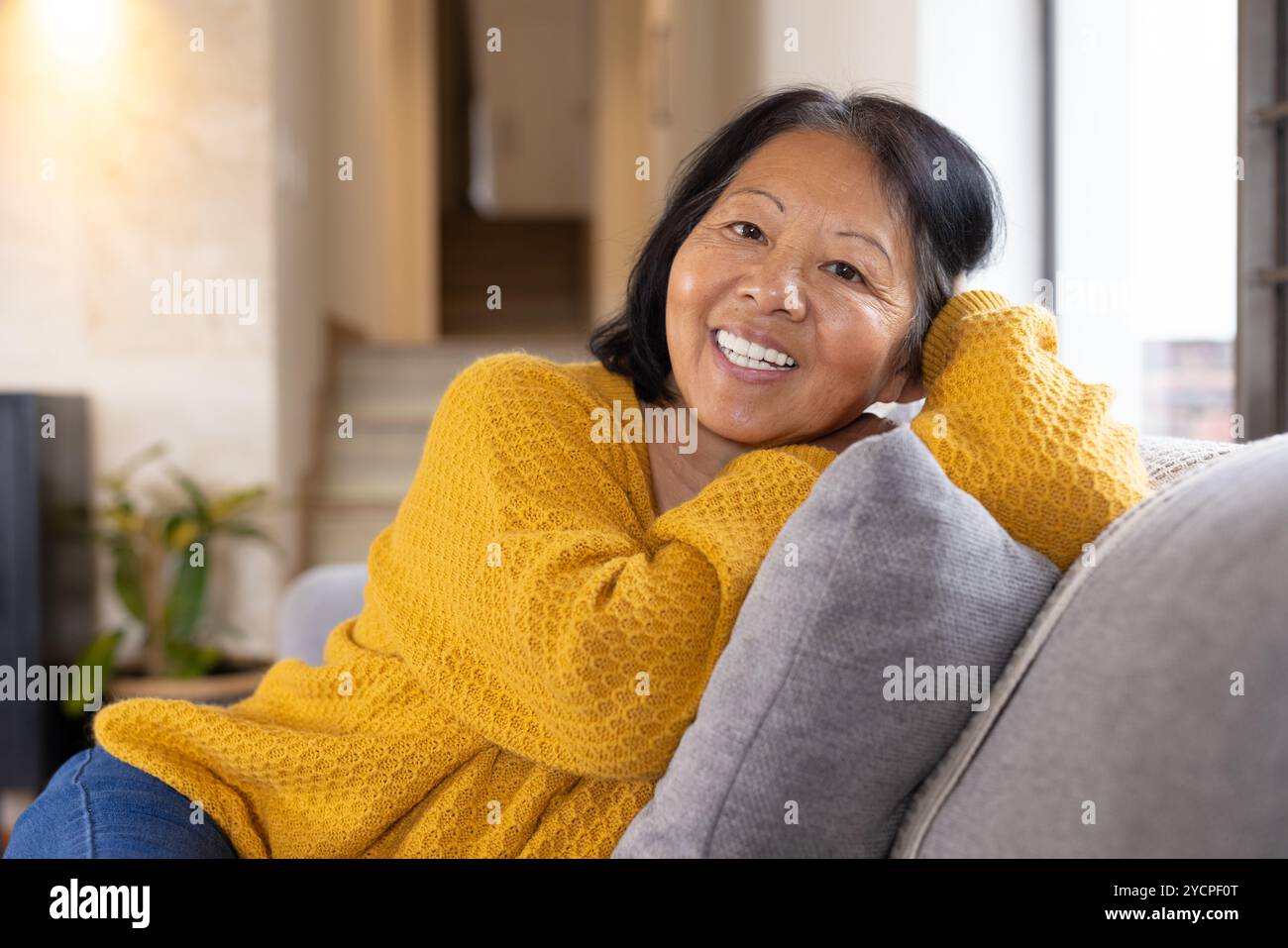 Donna asiatica sorridente che si rilassa sul divano a casa durante il periodo natalizio Foto Stock