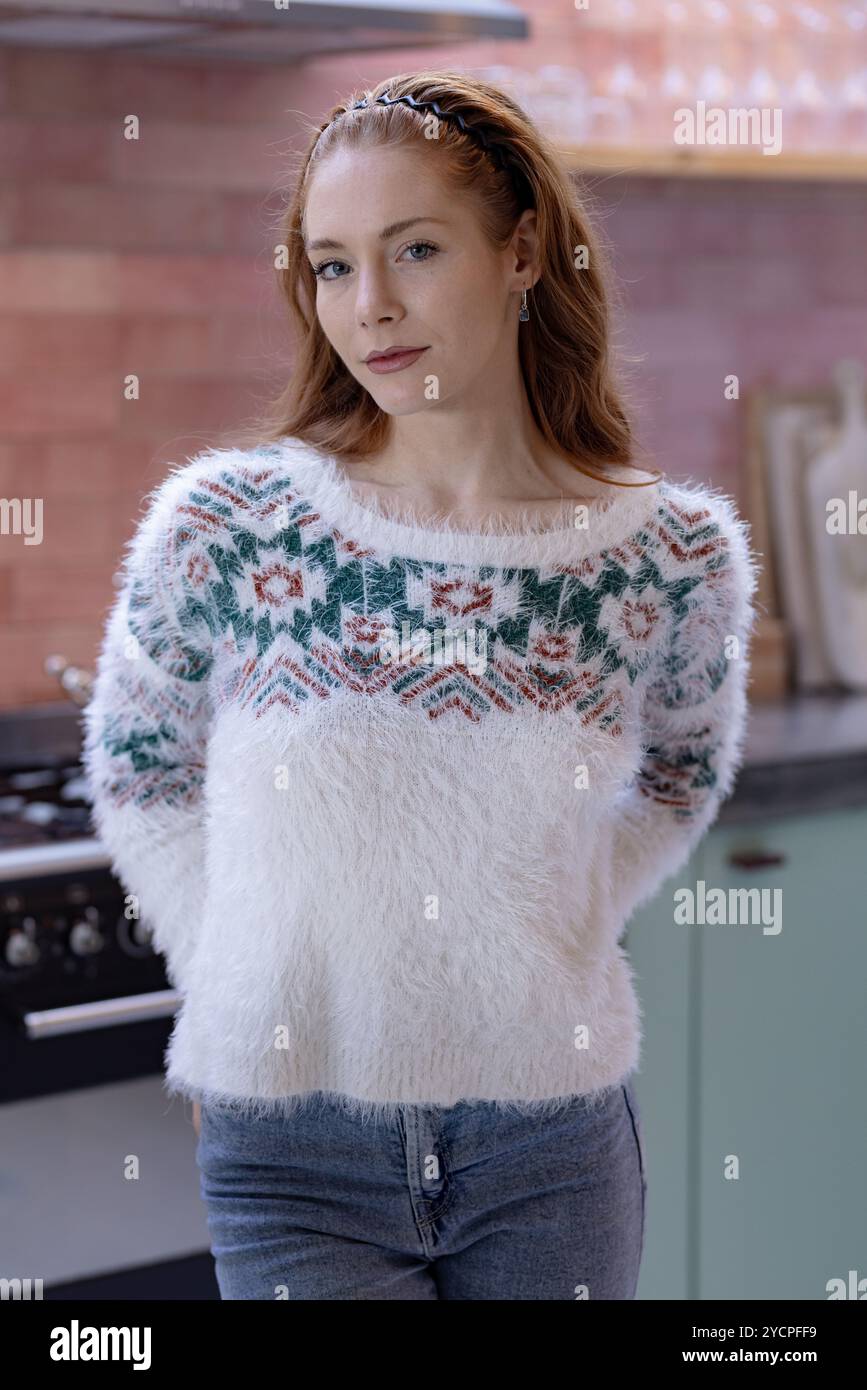 Natale, a casa, donna in un comodo maglione in piedi in cucina, con un aspetto contento e rilassato Foto Stock