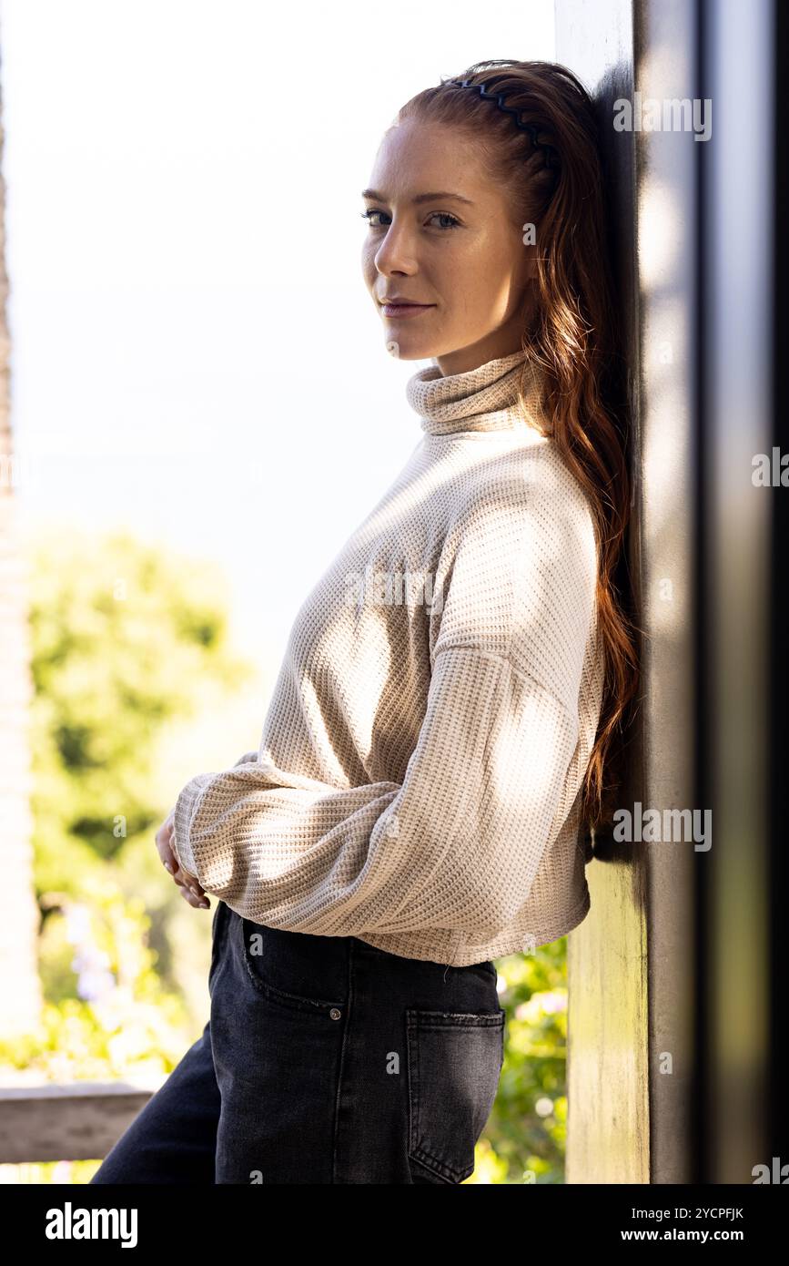 Donna in un comodo maglione appoggiata al muro, che gode di una tranquilla vista all'aperto Foto Stock