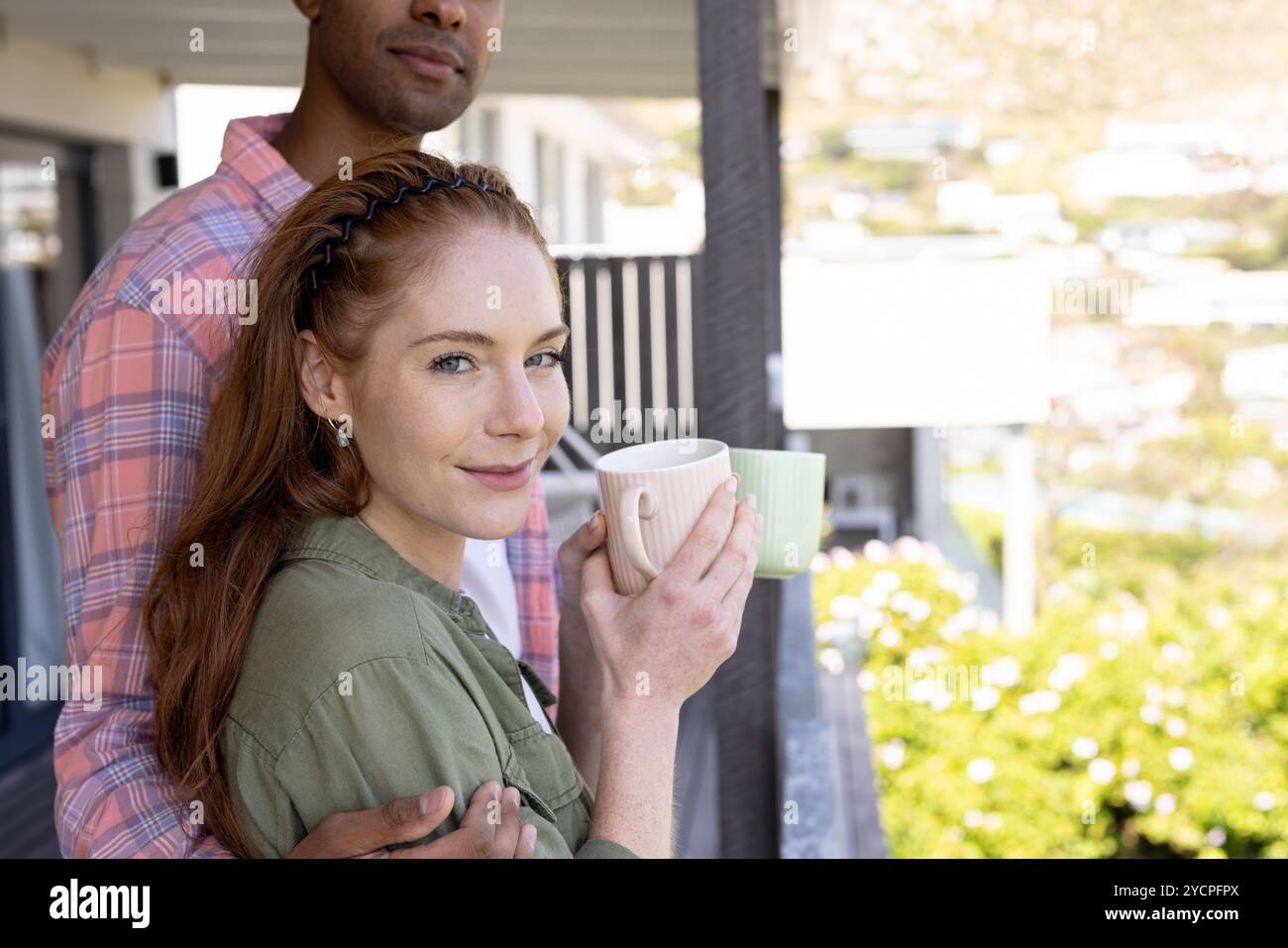 Coppia sorridente che si gusta un caffè sul balcone, abbracciando una mattinata tranquilla Foto Stock