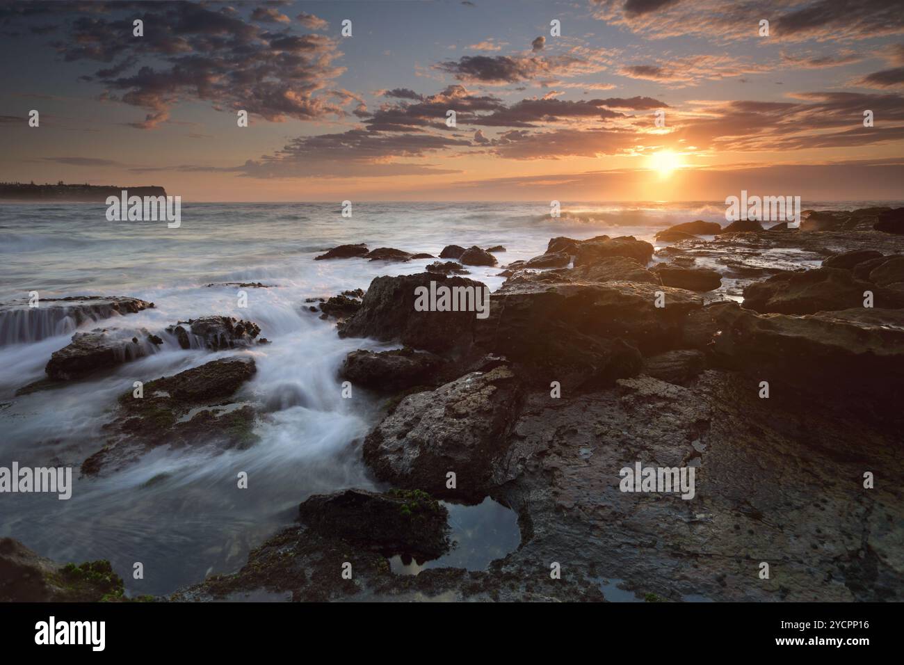 L'alba sulla spiaggia di Warriewood con la bassa marea, con i suoi dolci flussi e le graziose nuvole altocumulus oscurano parzialmente il sole, i suoi caldi raggi invernali evidenziano il wa Foto Stock