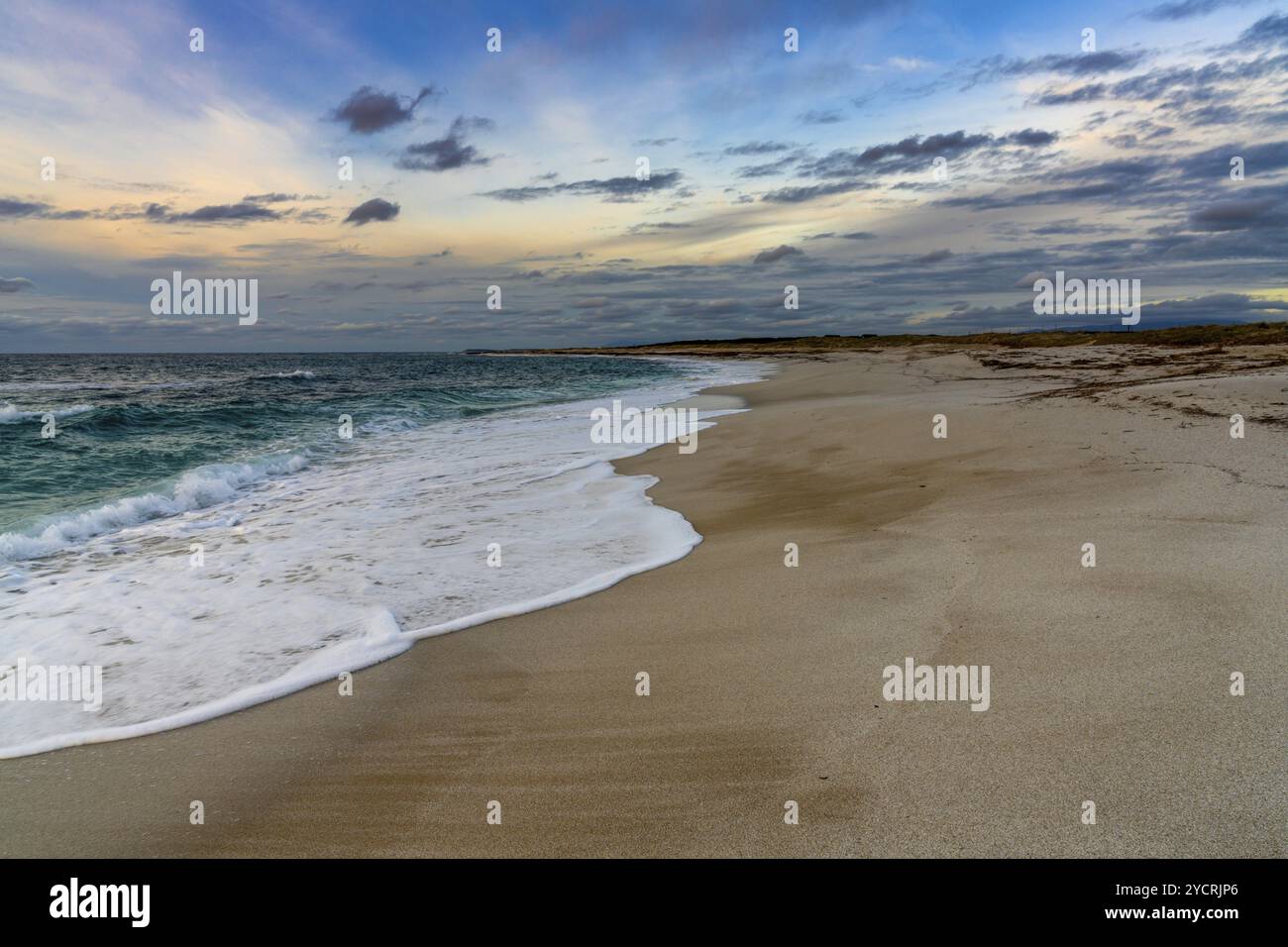 Una vista ad angolo basso della spiaggia di sabbia bianca con onde che si avvolgono sotto un colorato cielo del tramonto Foto Stock