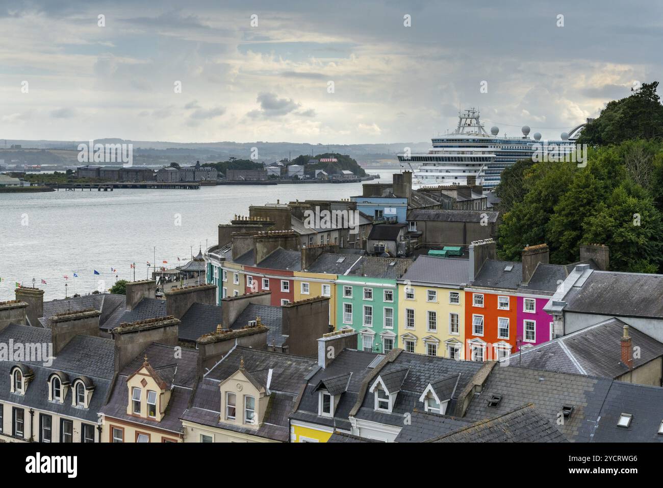 Cobh, Irlanda, 15 agosto 2022: Case colorate nel centro di Cobh con un'enorme nave da crociera ormeggiata nel porto di Cork, in Europa Foto Stock