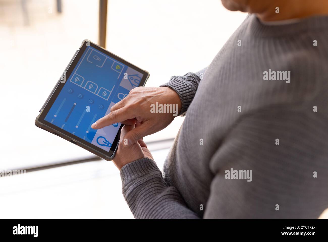 Uomo anziano asiatico che utilizza un tablet per controllare i dispositivi domestici intelligenti, regolando le impostazioni con facilità Foto Stock