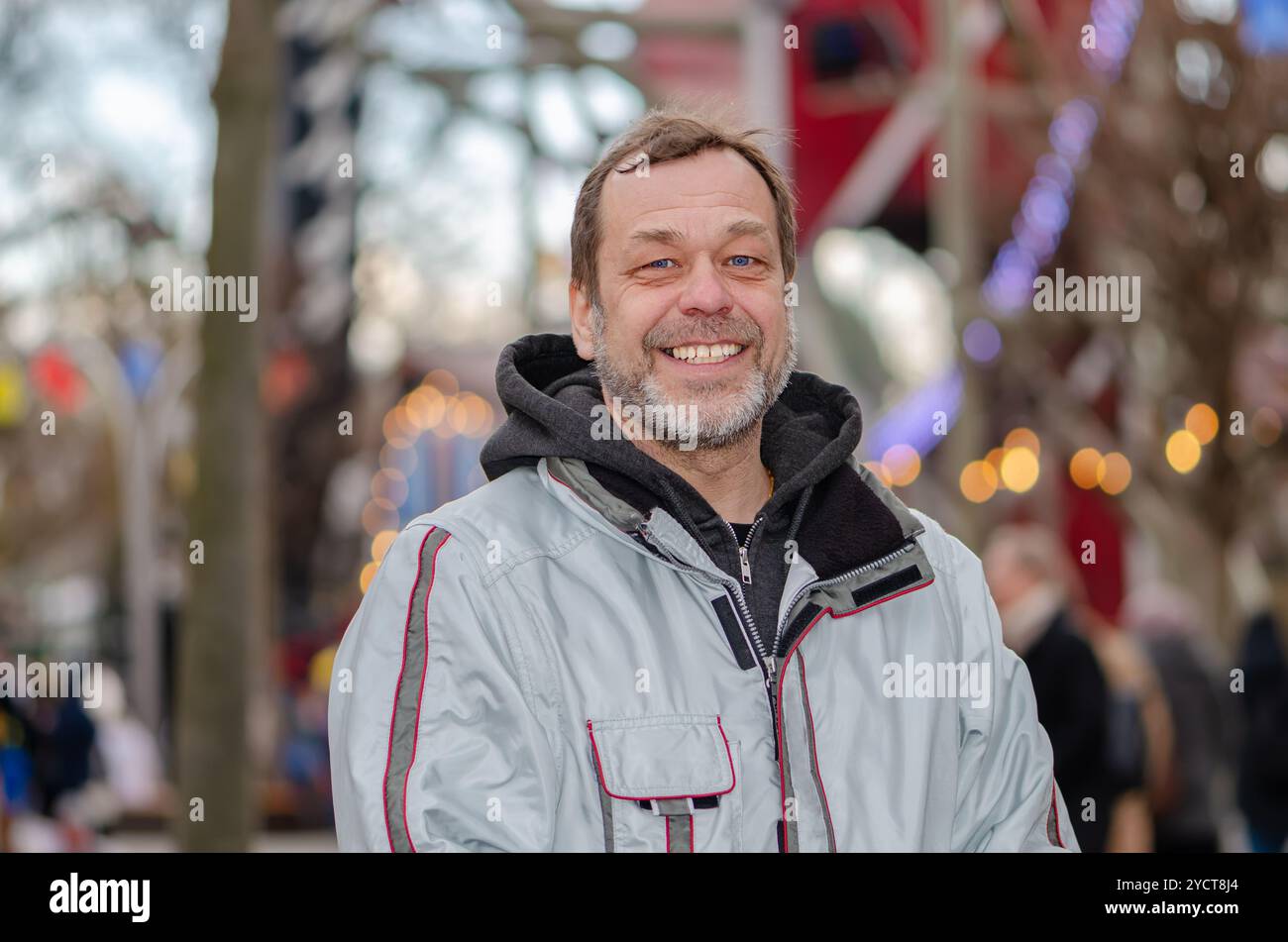 Ritratto di strada di un uomo sorridente di 50-55 anni in una giacca su uno sfondo sfocato tra le persone. Foto Stock