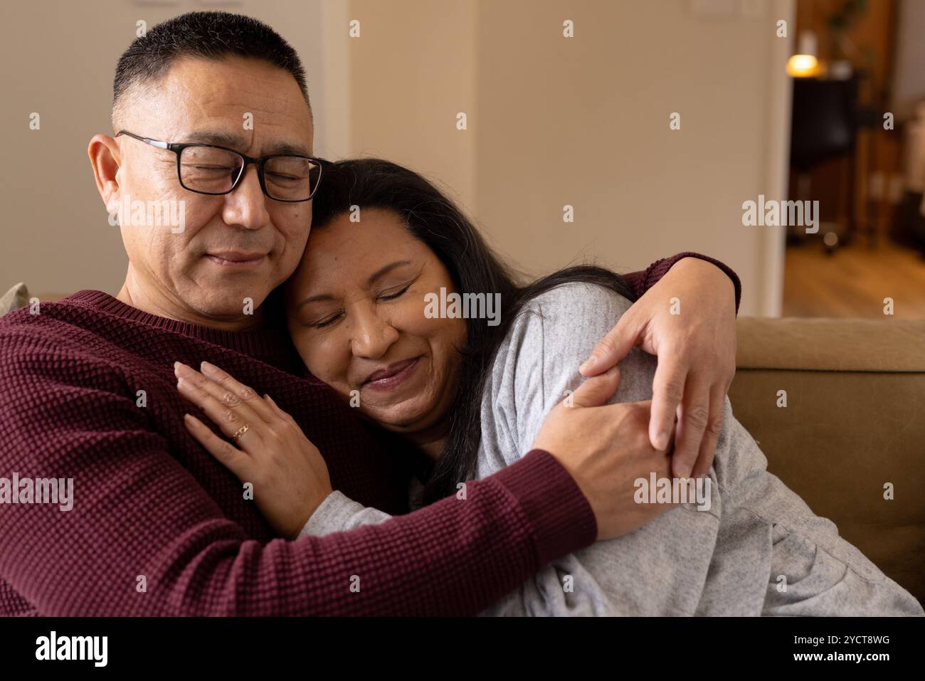 Coppia senior multirazziale che abbraccia su un comodo divano, condividendo caldi momenti di vacanza a casa Foto Stock