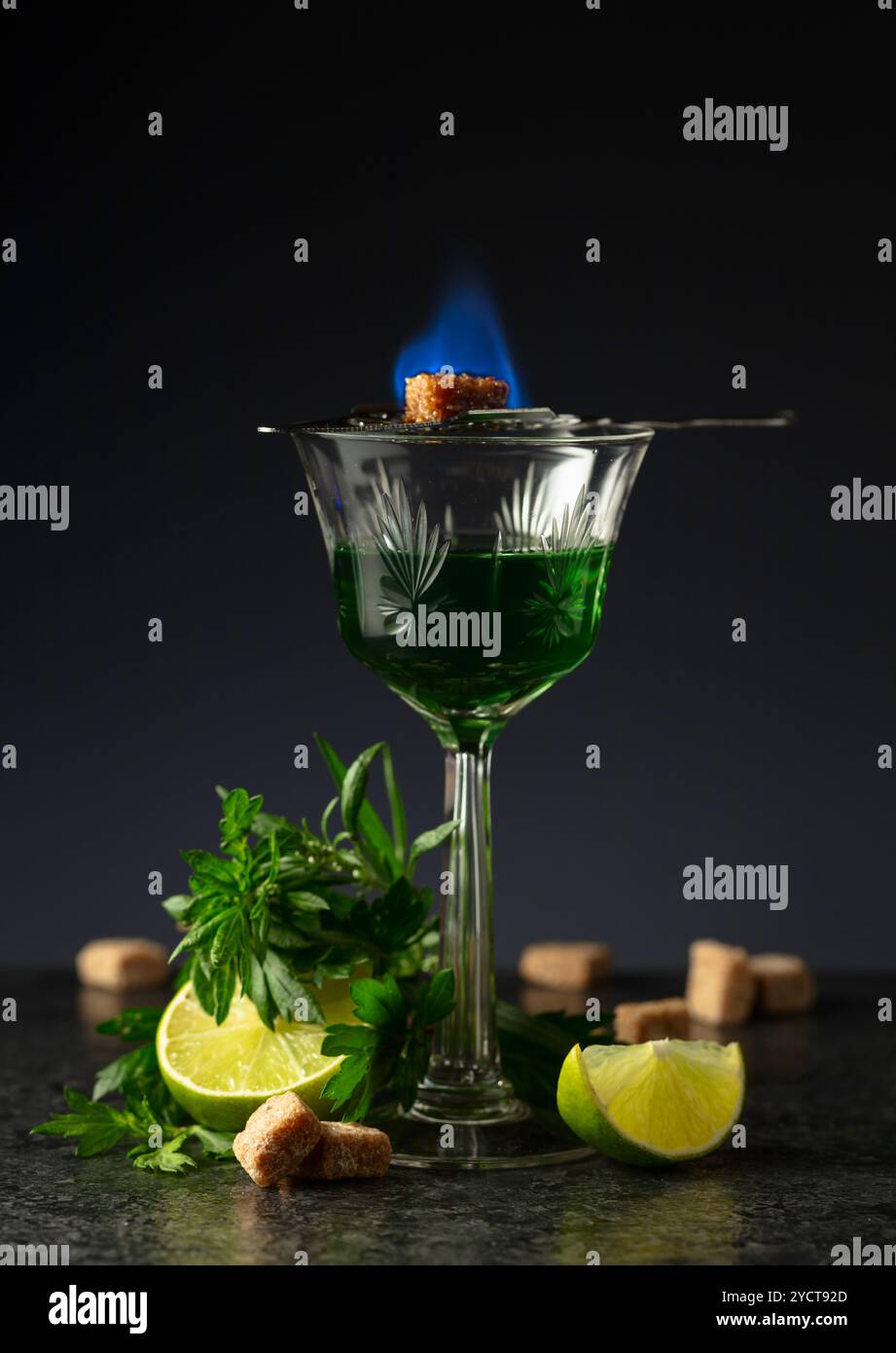 Bruciare lo zucchero su un bicchiere con assenzio. Preparazione della bevanda. Absinthe con ingredienti su sfondo nero. Foto Stock