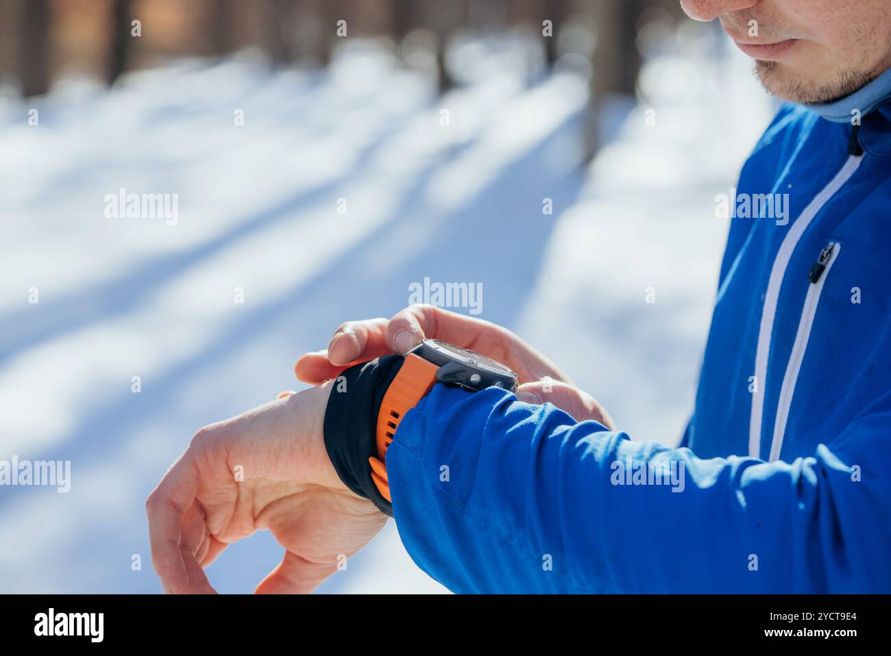 Il corridore in una foresta innevata si prende una pausa per controllare il suo smartwatch, analizzando i dati sulla frequenza cardiaca e sui progressi in inverno Foto Stock