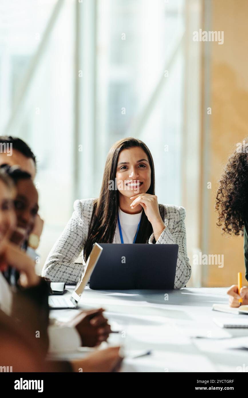 Una donna professionista sicura di sé che conduce una discussione di marketing di gruppo in un ambiente di ufficio moderno. Sono coinvolti partecipanti diversi, mettendo in evidenza il team Wo Foto Stock