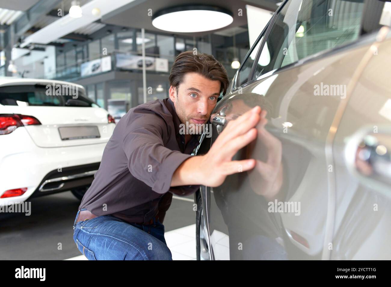 Concessionaria auto - giovane e affascinante uomo controlla la qualità della vernice della nuova vettura Foto Stock
