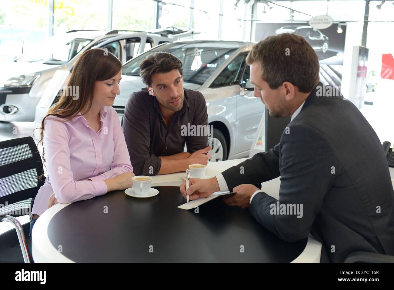 Coppia giovane l'acquisto di una nuova auto nello showroom di una concessionaria auto - firma del contratto di vendita con il venditore Foto Stock
