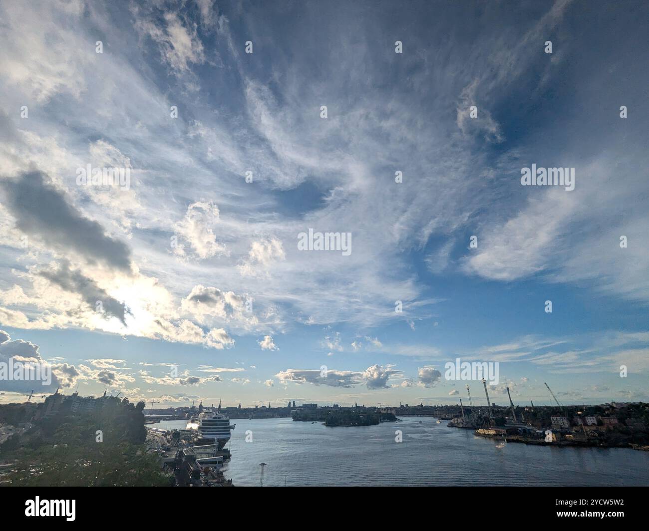 Ampia vista su una baia della città con barche e un ampio cielo blu con nuvole ondulate. - Immagine stock catturata con smartphone