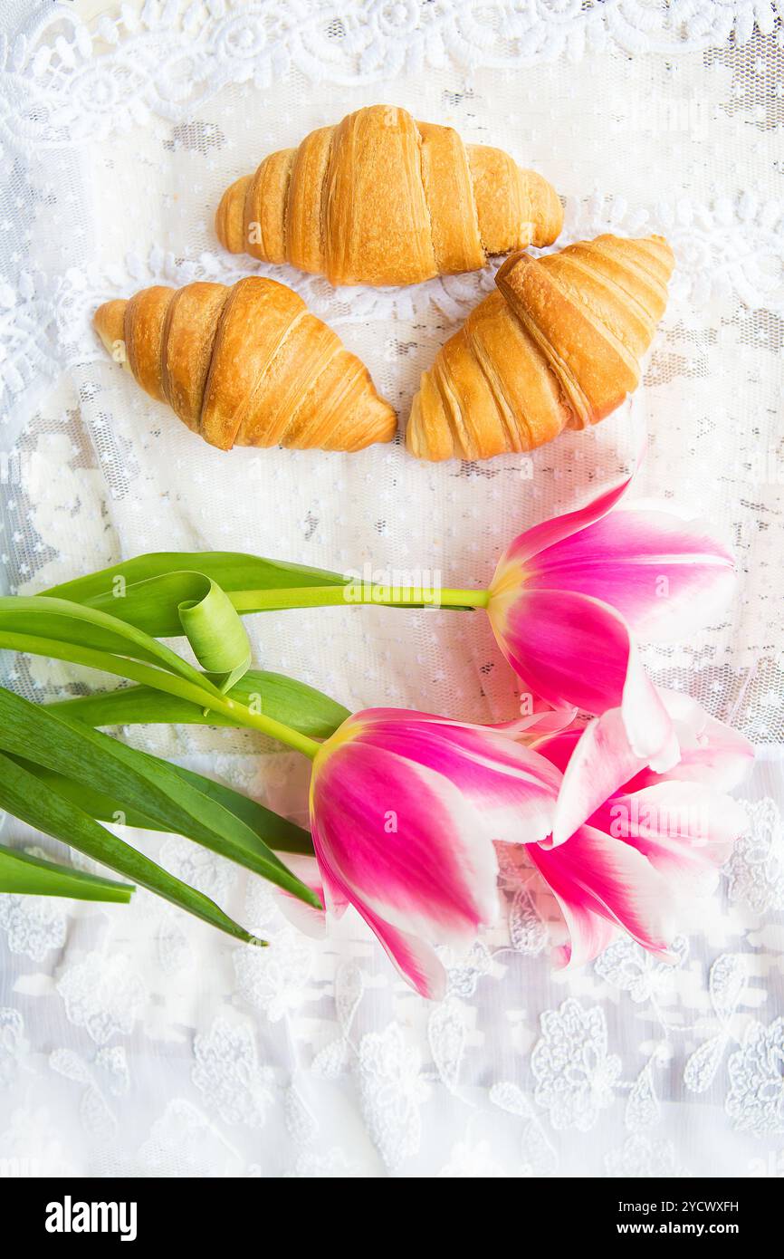 Tre croissant e rosa luminoso tulipani sulla tovaglia di pizzo Foto Stock