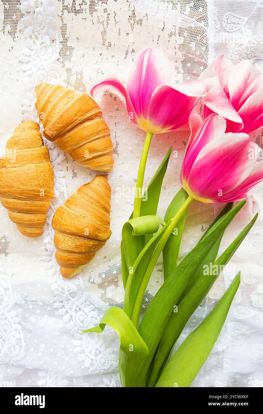 Tre croissant e rosa luminoso tulipani sulla tovaglia di pizzo Foto Stock