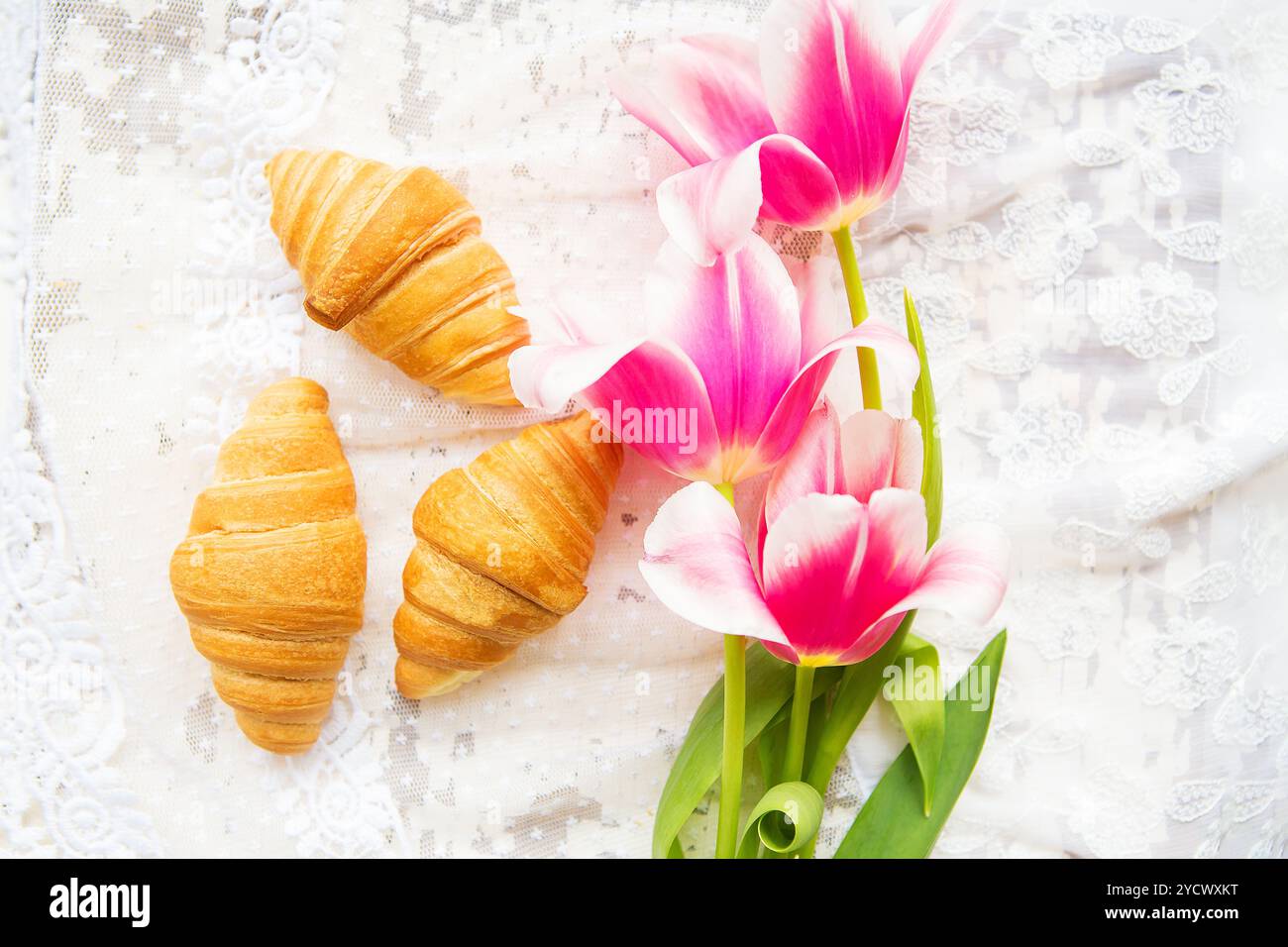 Tre croissant e rosa luminoso tulipani sulla tovaglia di pizzo, close-up Foto Stock