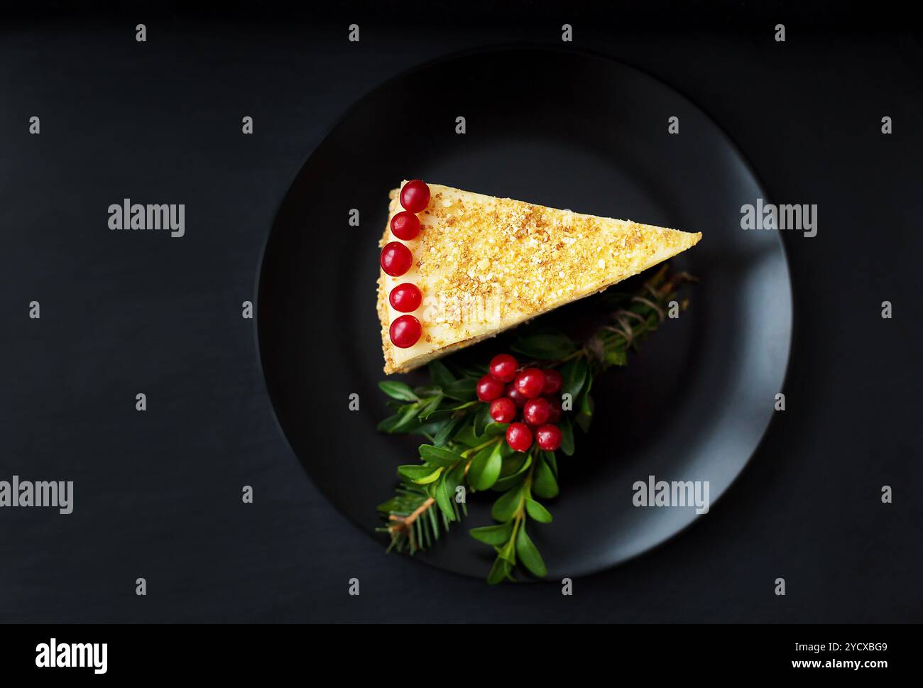 Fetta di torta decorata con albero di Natale e frutti di bosco rossi su sfondo nero Foto Stock