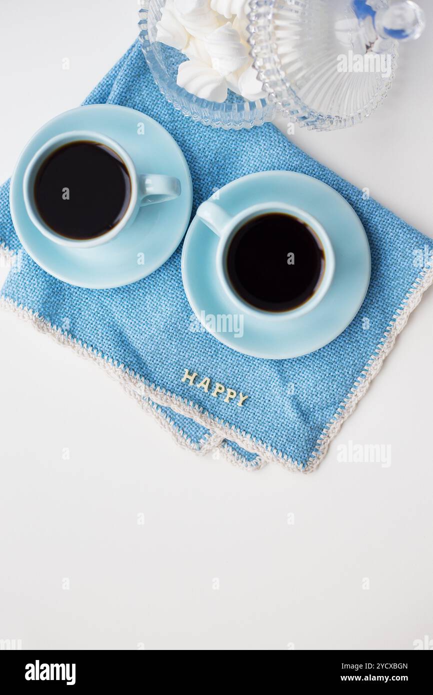 Due tazze di caffè blu su tovagliolo blu con la scritta "Happy" Foto Stock