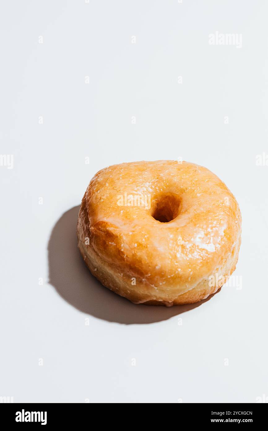 Immagine di una ciambella lucida e vegana glassata con zucchero su uno sfondo bianco, che mostra la sua finitura dolce, liscia e lucida sulla parte superiore Foto Stock