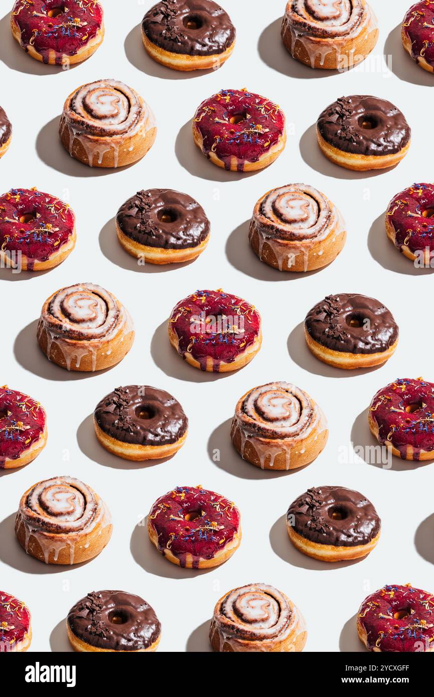 Una disposizione artistica di ciambelle vegane e dolci alla cannella con glassa al cioccolato, glassa ai frutti di bosco e glassa, questo vivace motivo mette in mostra una varietà Foto Stock