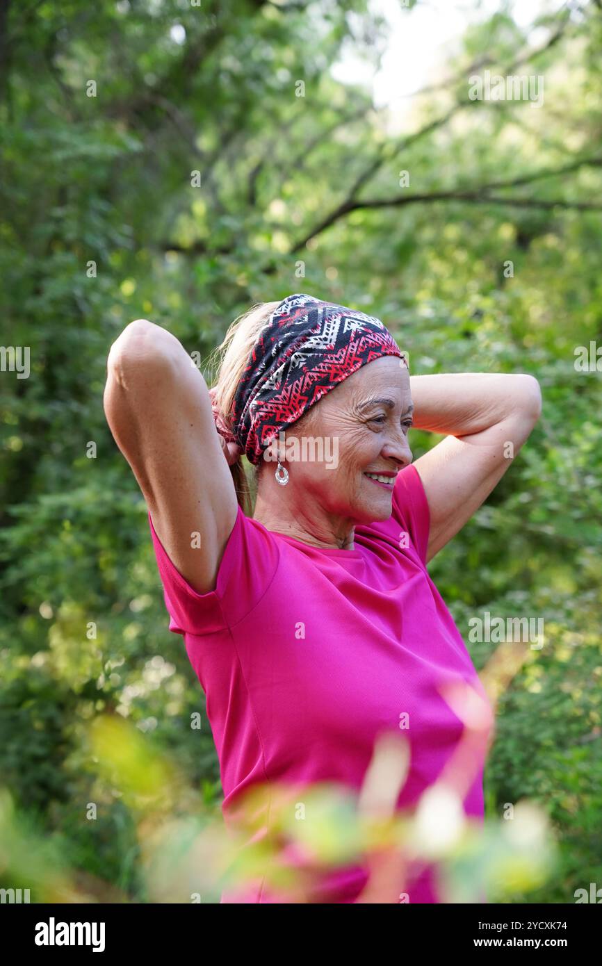 Una donna allegra e matura con un archetto colorato mette i capelli in una coda di cavallo, sorridendo ampiamente e mostrando uno stile di vita attivo Foto Stock