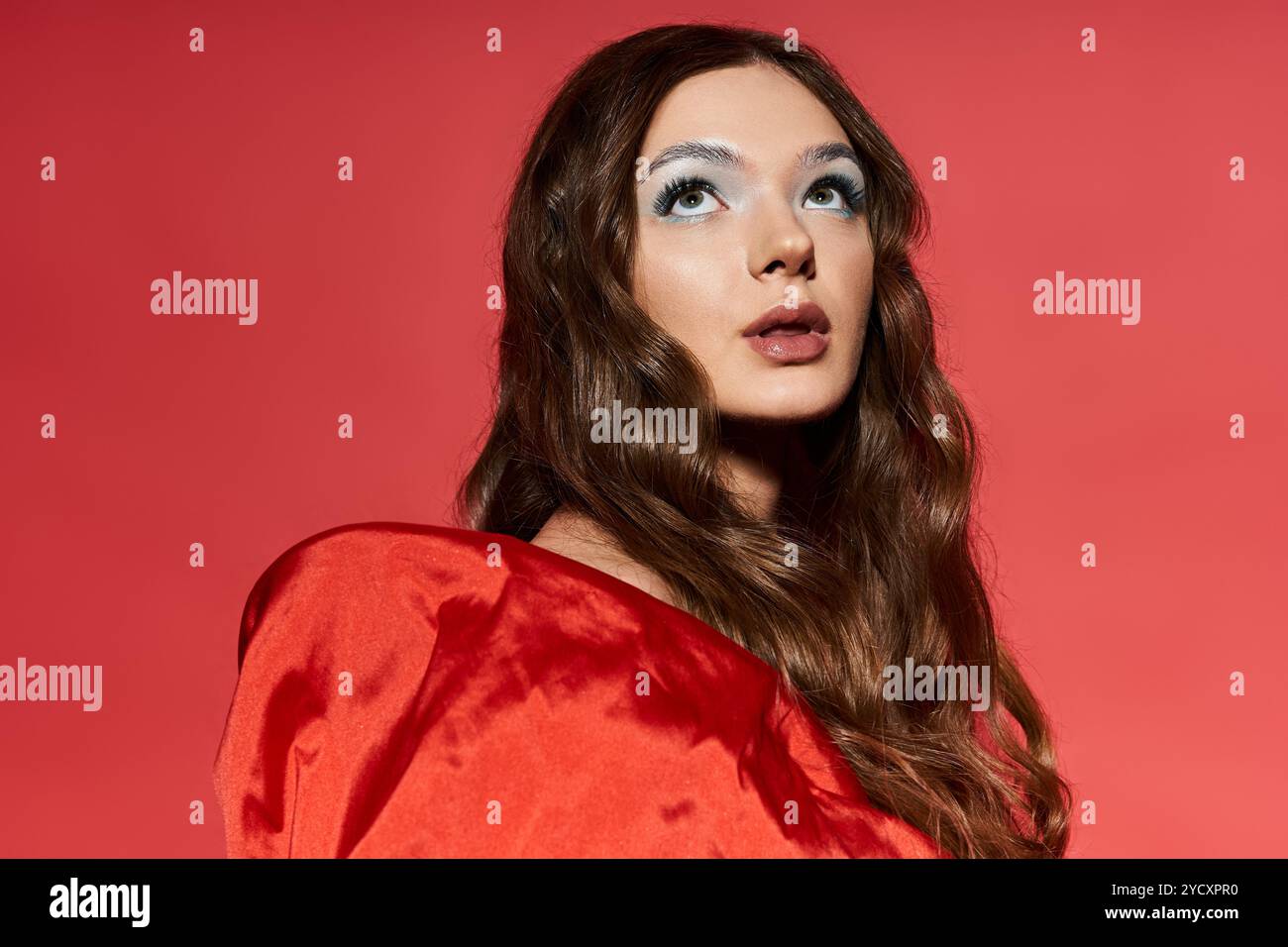 Una bella giovane donna guarda attentamente verso l'alto indossando un look rosso. Foto Stock