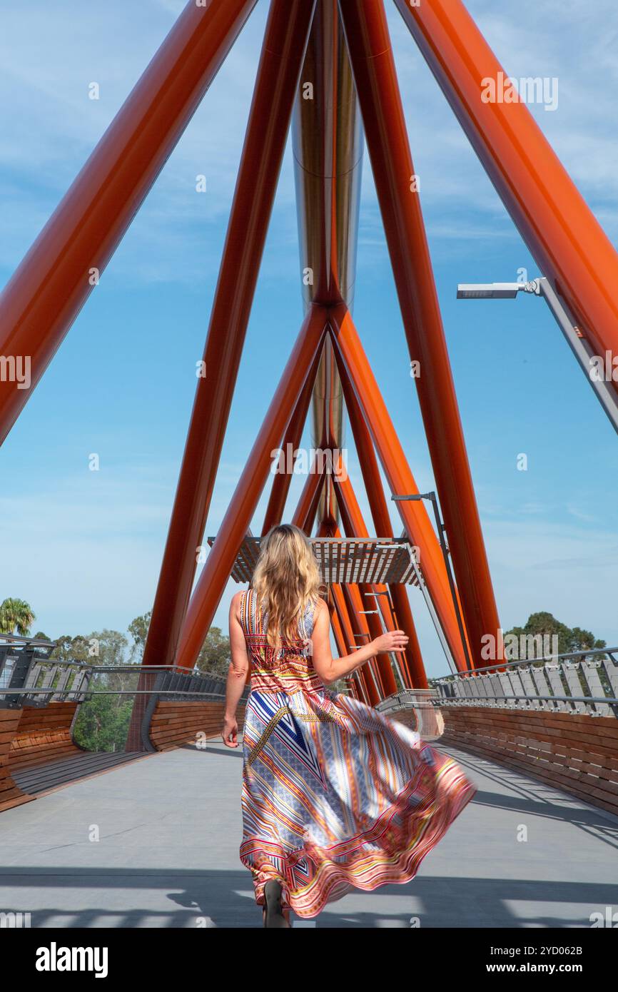 Una donna sgargiante con un lungo prendisole dai colori vivaci e fantasia cammina attraverso Yandhai Nepean Crossing, un nuovo ponte con il nome aborigeno di Darug me Foto Stock