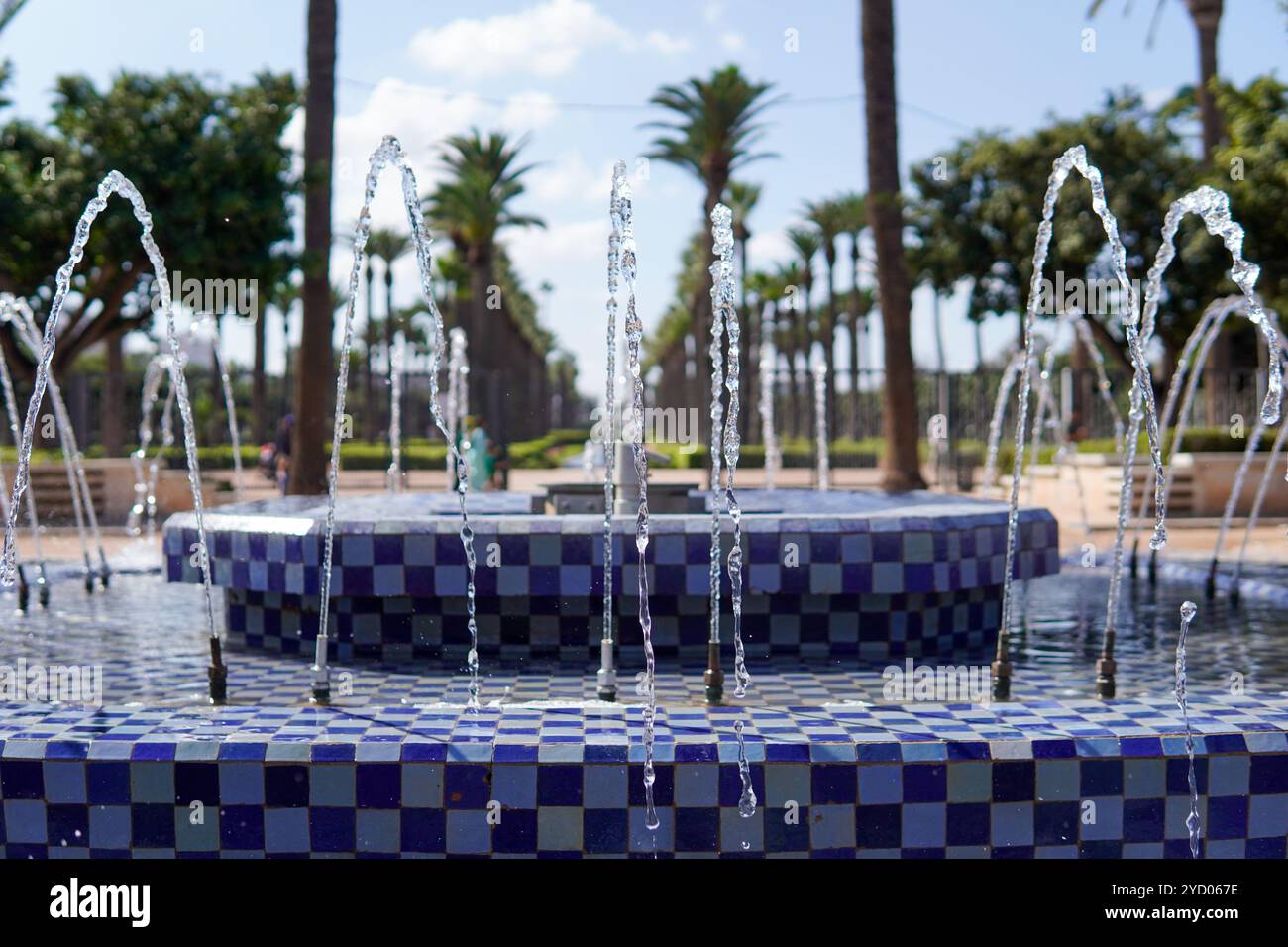 Una fontana ornata con piastrelle blu e bianche, con diversi getti d'acqua che si arcano graziosamente. Sullo sfondo, palme e un cielo azzurro Foto Stock