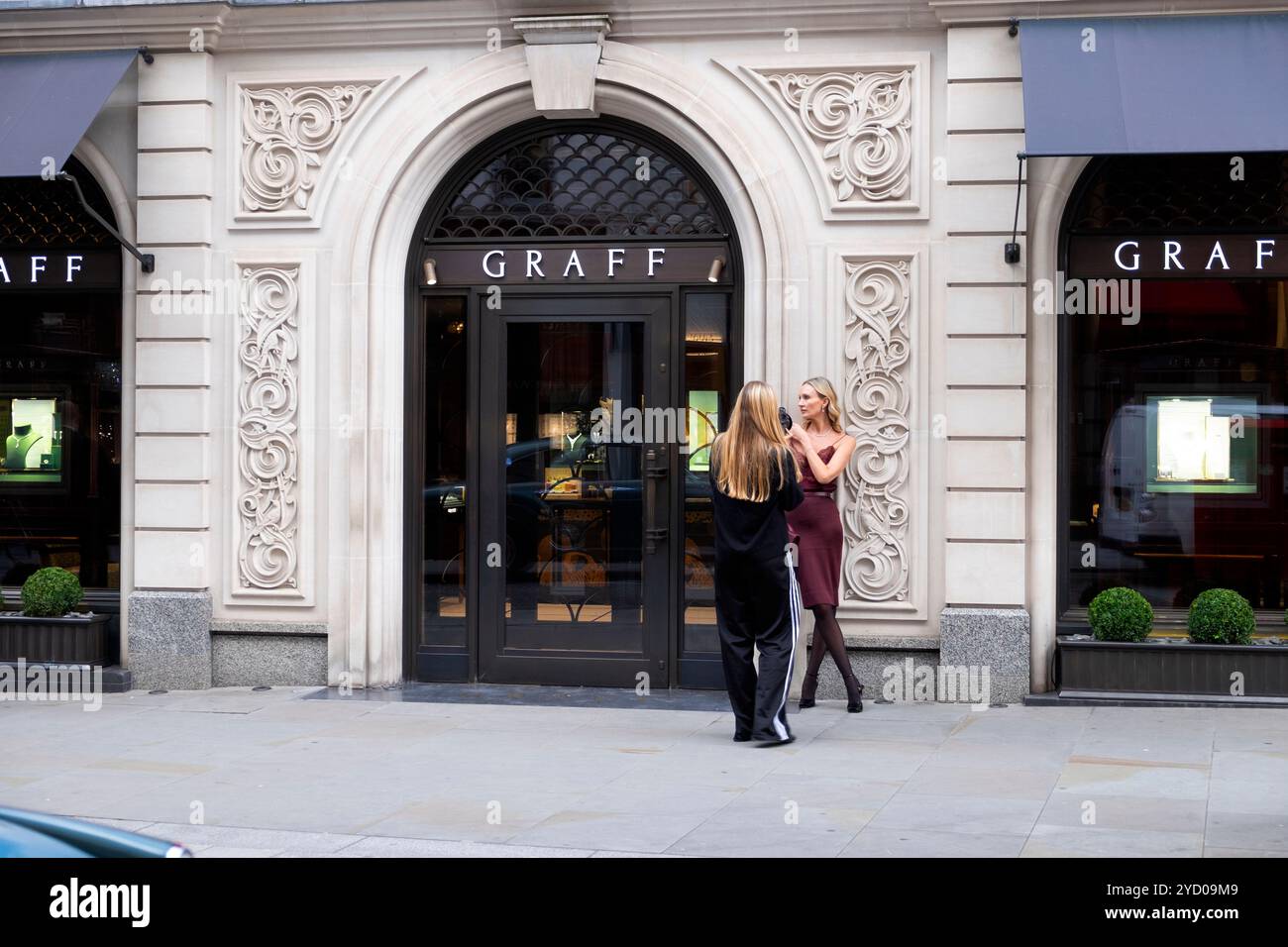 Fotografa giovane donna che fotografa una modella donna anziana fuori dalla gioielleria GRAFF in New Bond Street a Londra W1 Inghilterra Regno Unito KATHY DEWITT Foto Stock