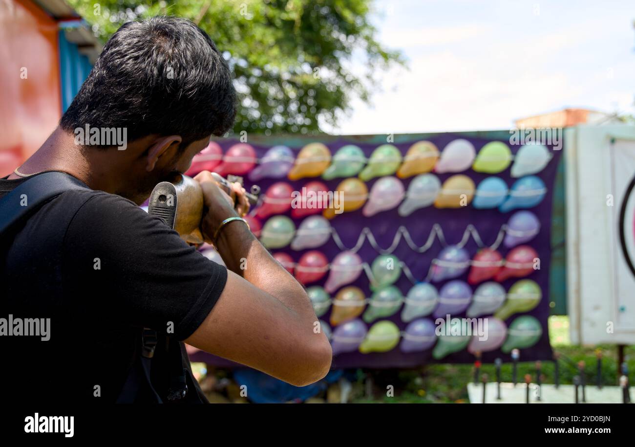 Un giovane prende di mira un bersaglio colorato di palloncini, mettendo alla prova le sue abilità in un gioco di tiro in fiera. Foto Stock