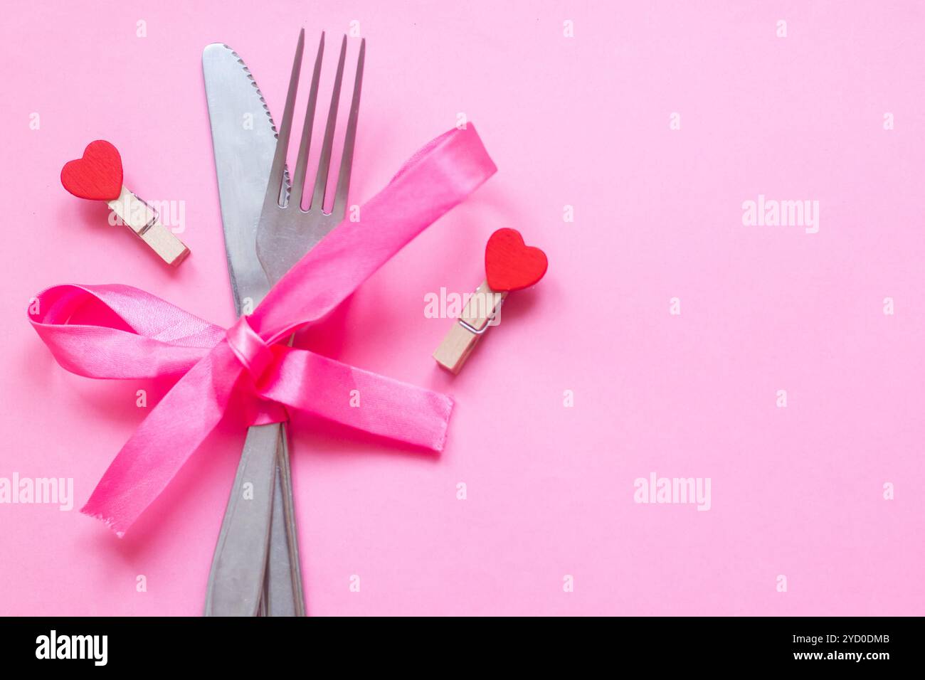 Cucchiaio con una forchetta legata con un nastro su sfondo rosa. Posate. Foto Stock